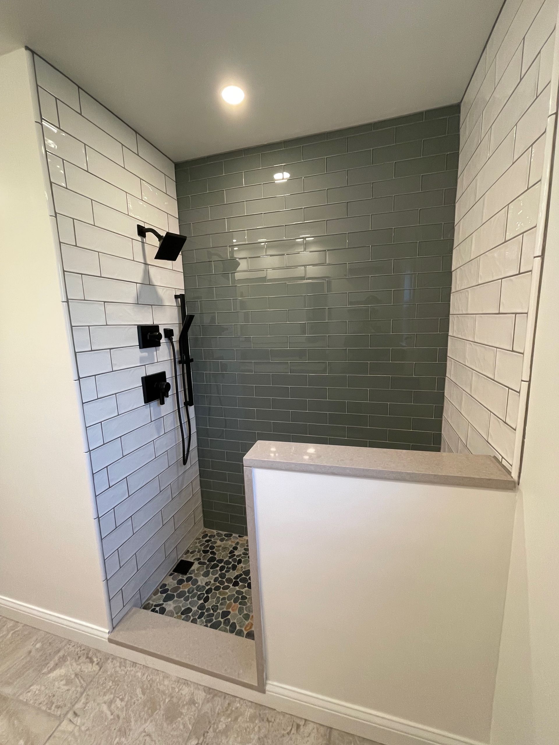 Modern walk-in shower with gray and white tile, black fixtures, and stone floor.