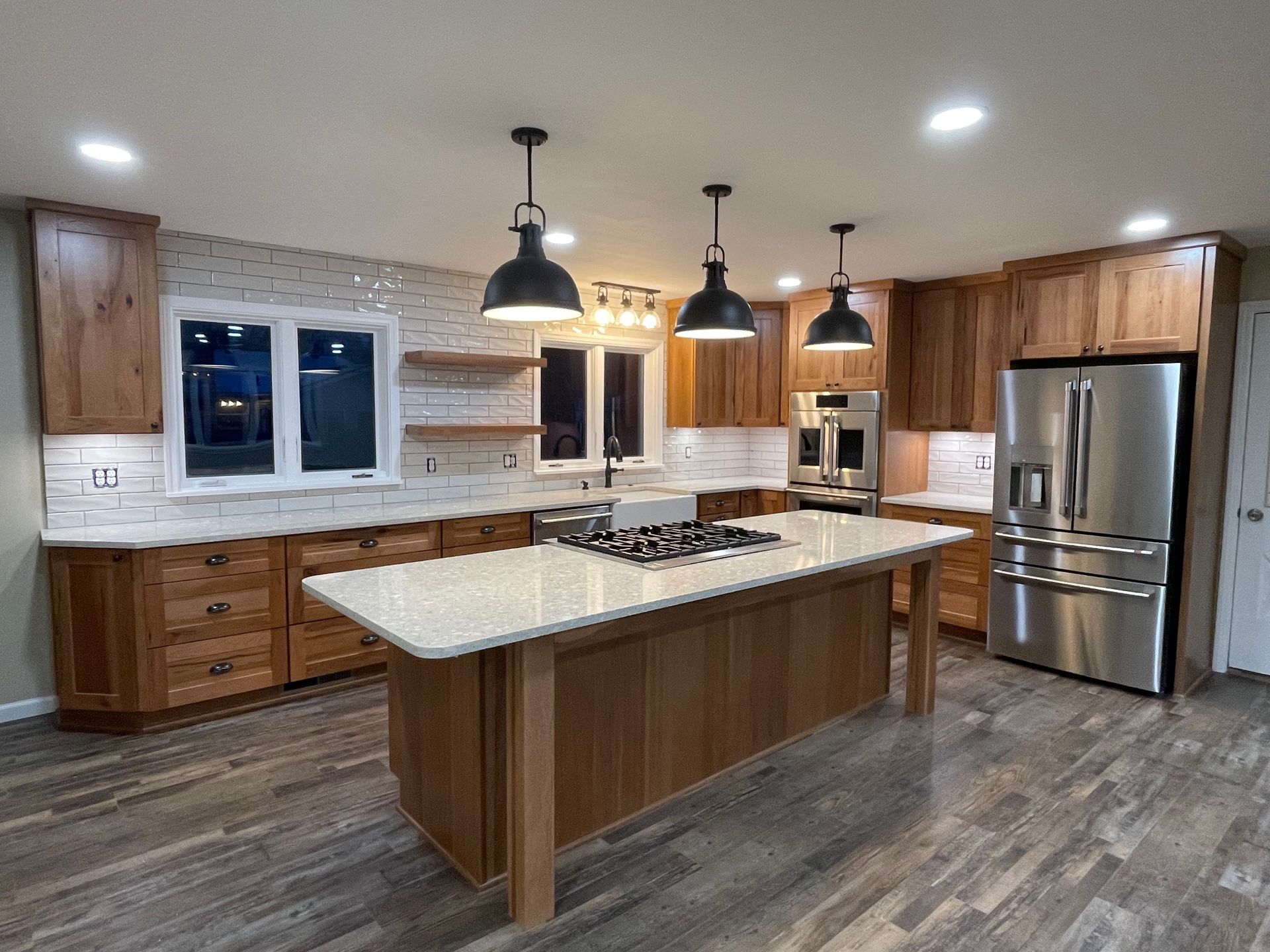 Spacious kitchen with wood cabinets, white countertops, stainless steel appliances, and island with cooktop.
