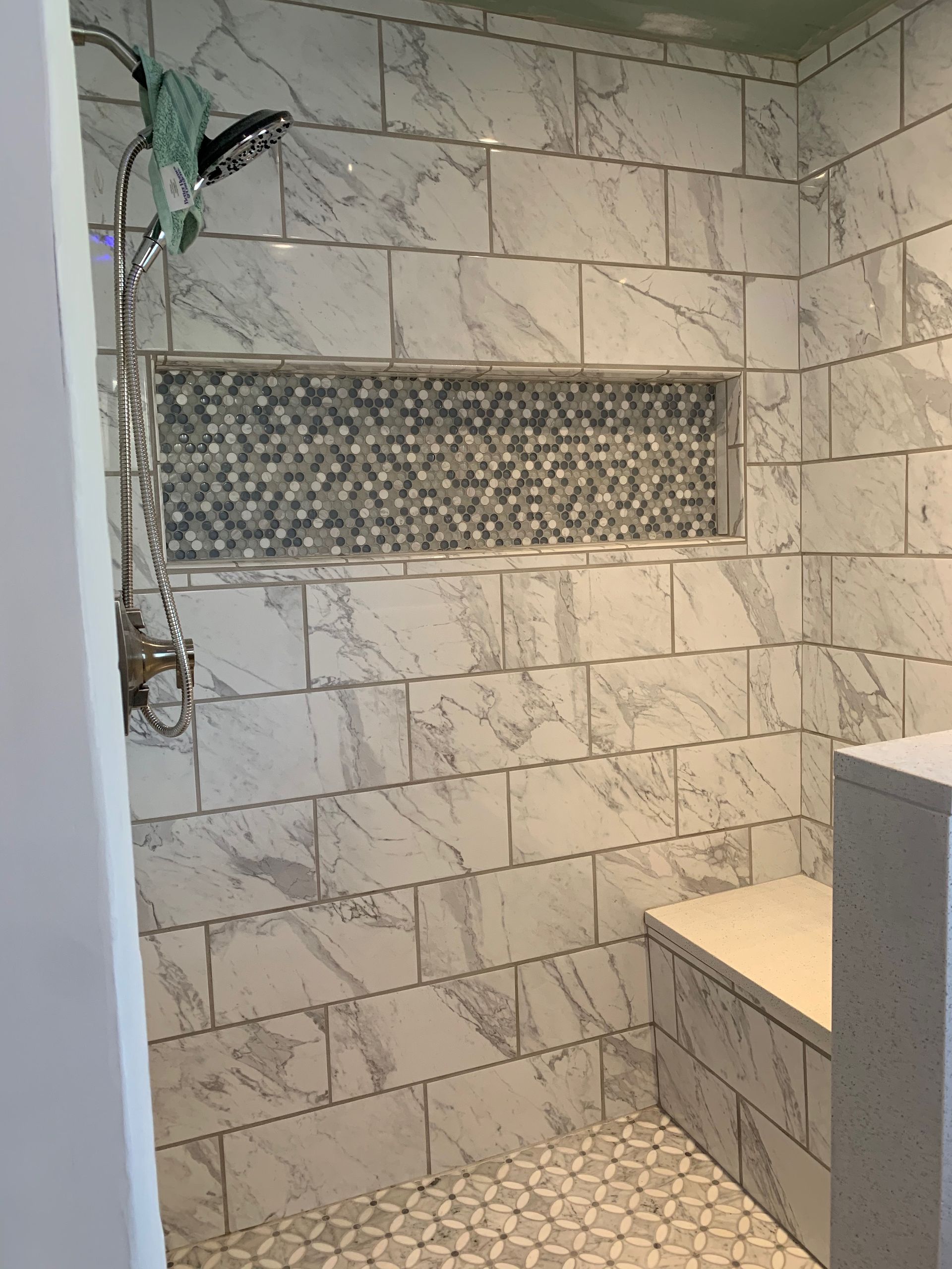 Tiled shower with a built-in bench and recessed shelf. The walls are white and gray marble.