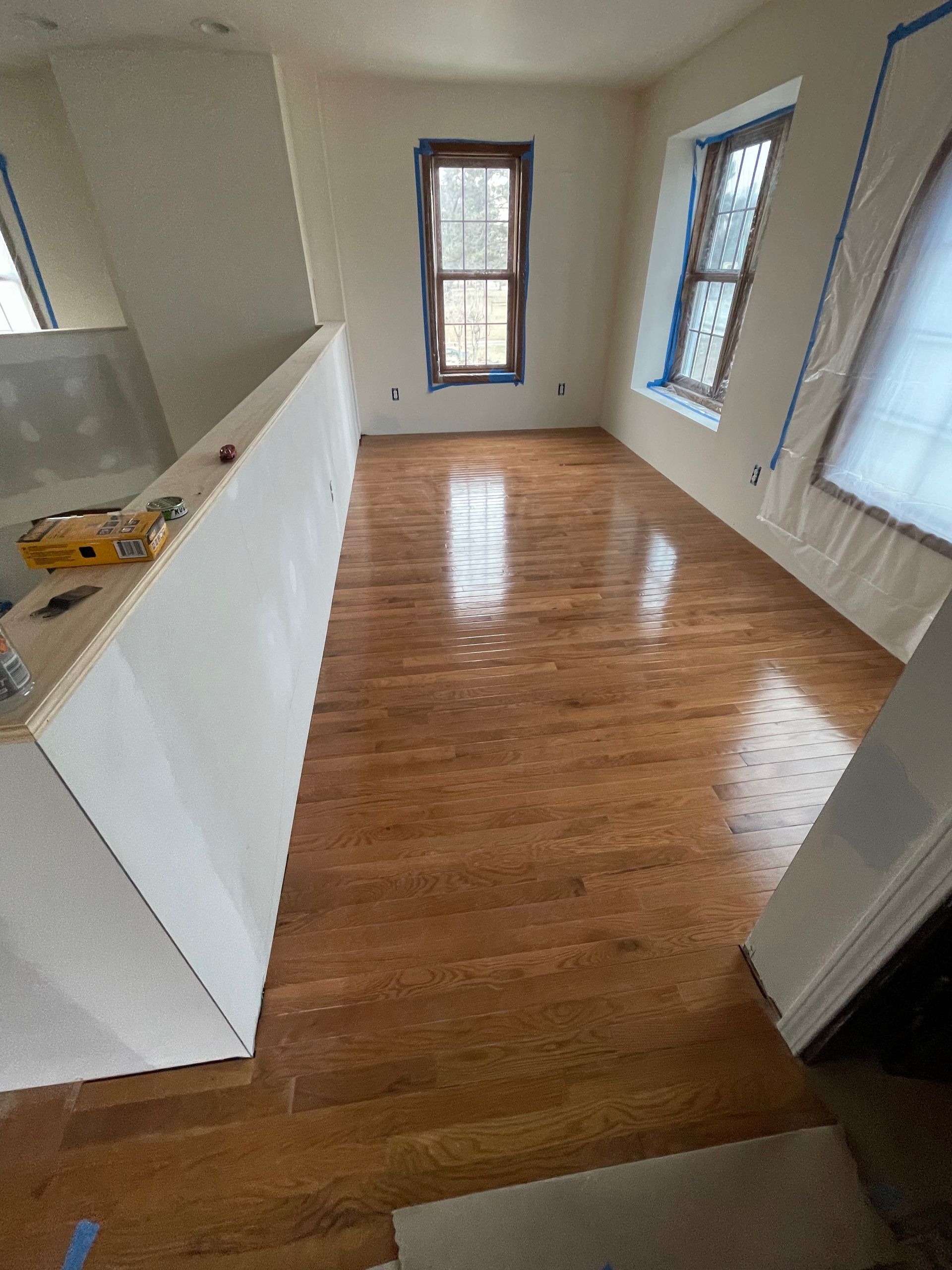 Newly finished hardwood floor in a room with windows and a white wall, reflecting light.