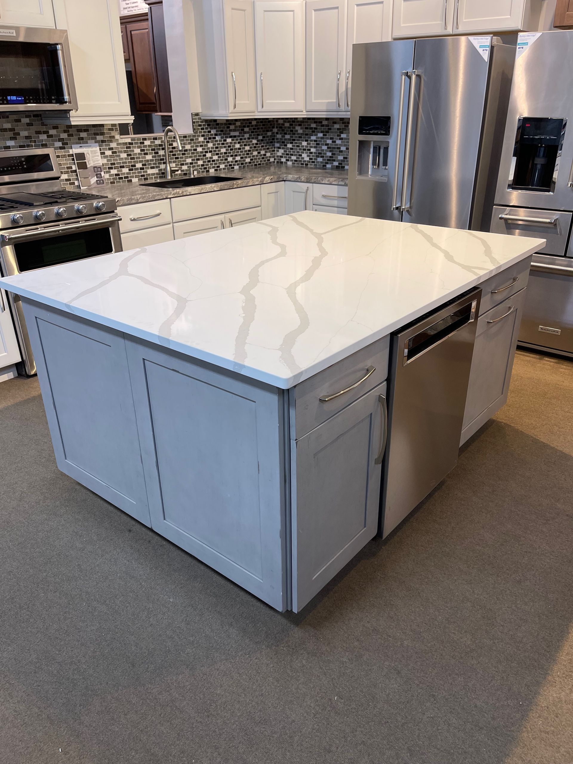 Kitchen island with white countertop, gray cabinets, stainless steel dishwasher.