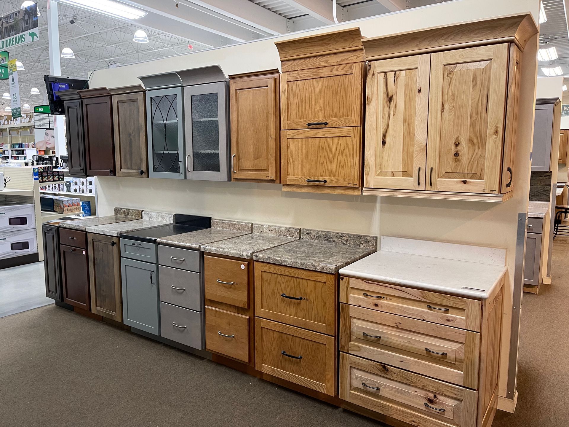 Kitchen cabinet displays showcasing various styles, wood finishes, and countertops in a store setting.