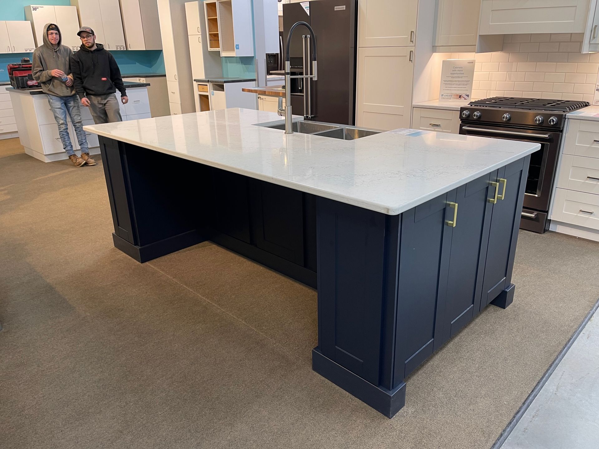Navy blue kitchen island with white countertop, sink, and gold hardware. Two people stand nearby.