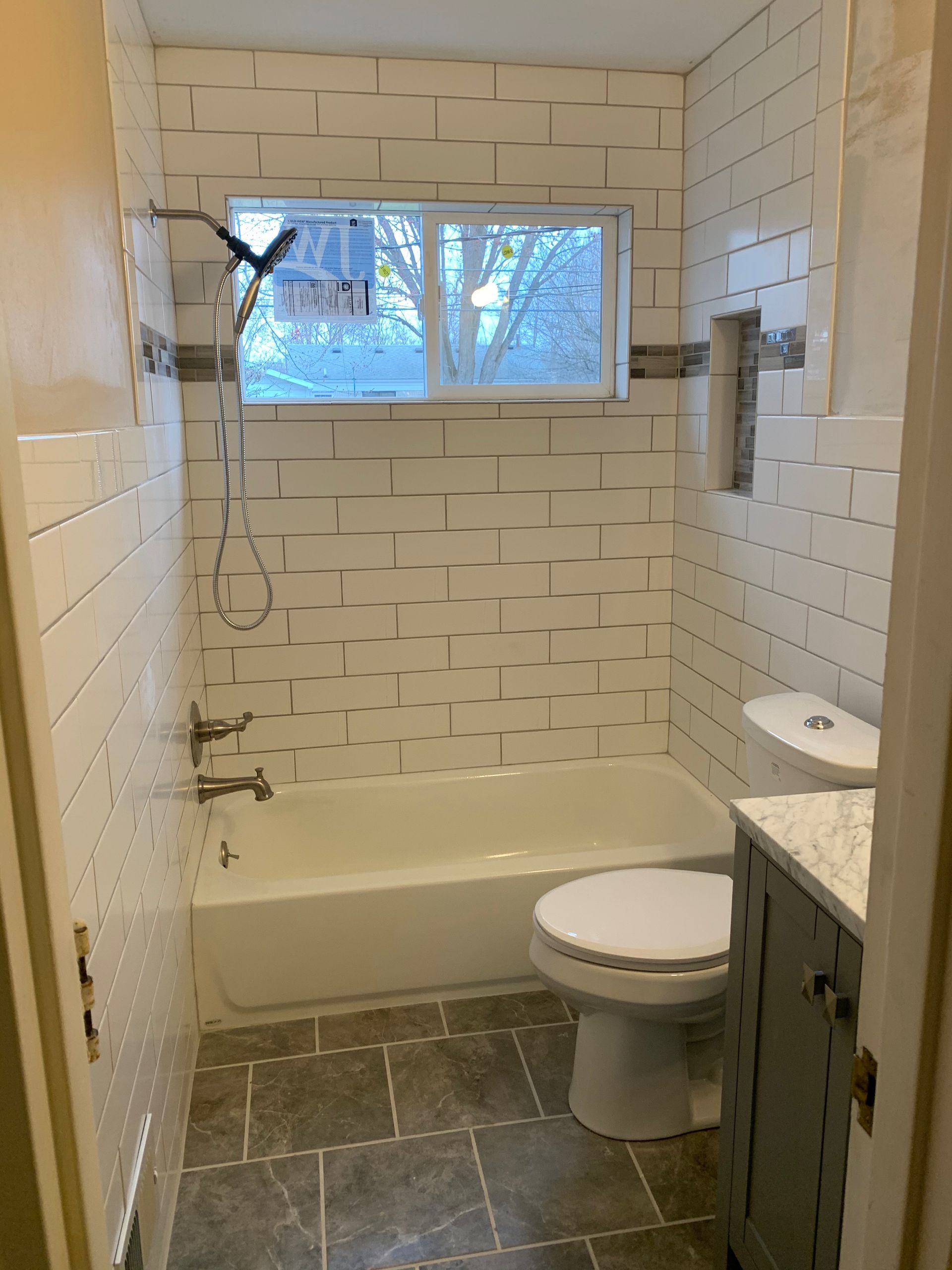 Bathroom with white subway tile, a tub, toilet, and gray vanity.