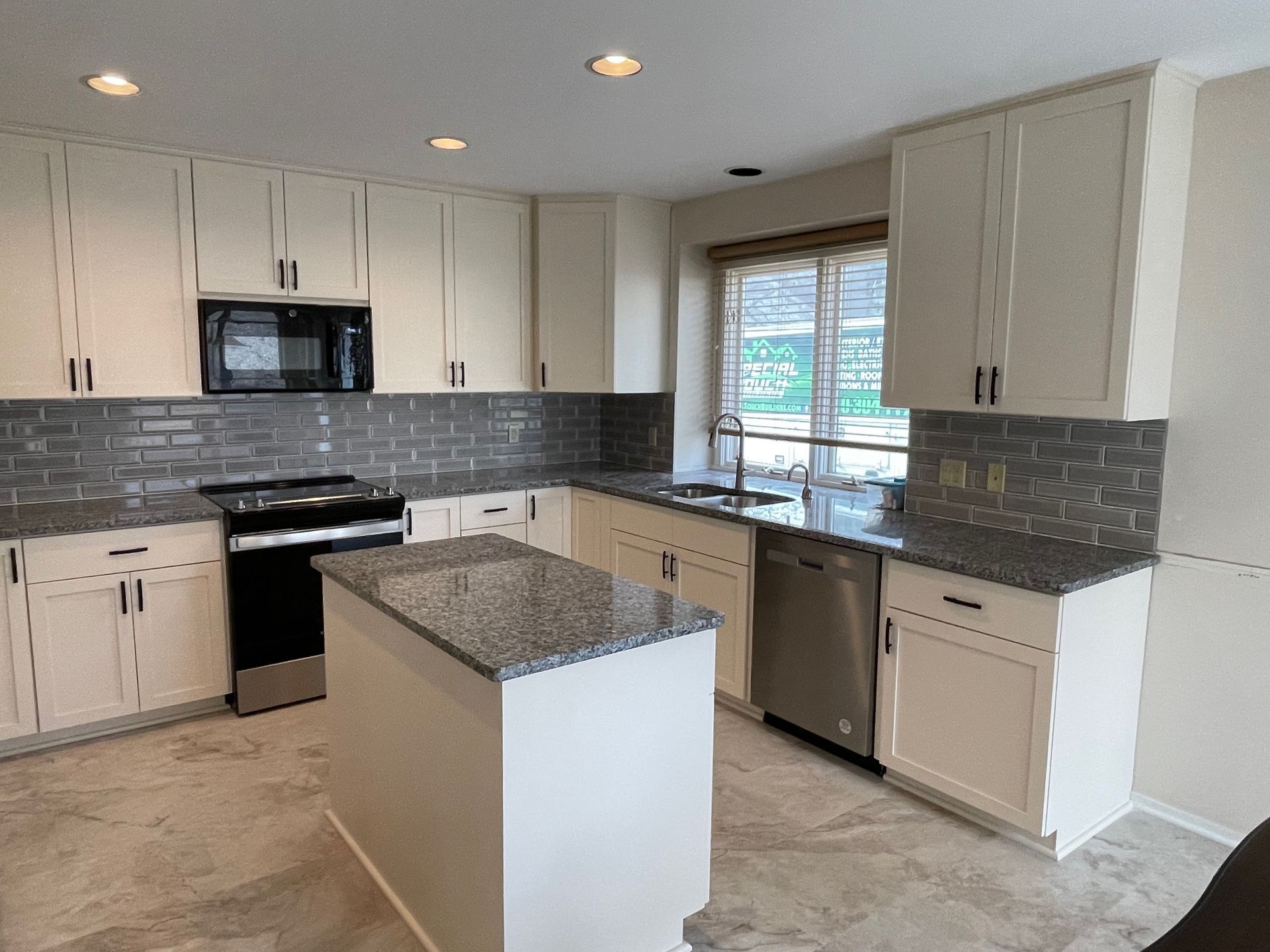 Kitchen with white cabinets, dark countertops, stainless steel appliances, and a gray backsplash.