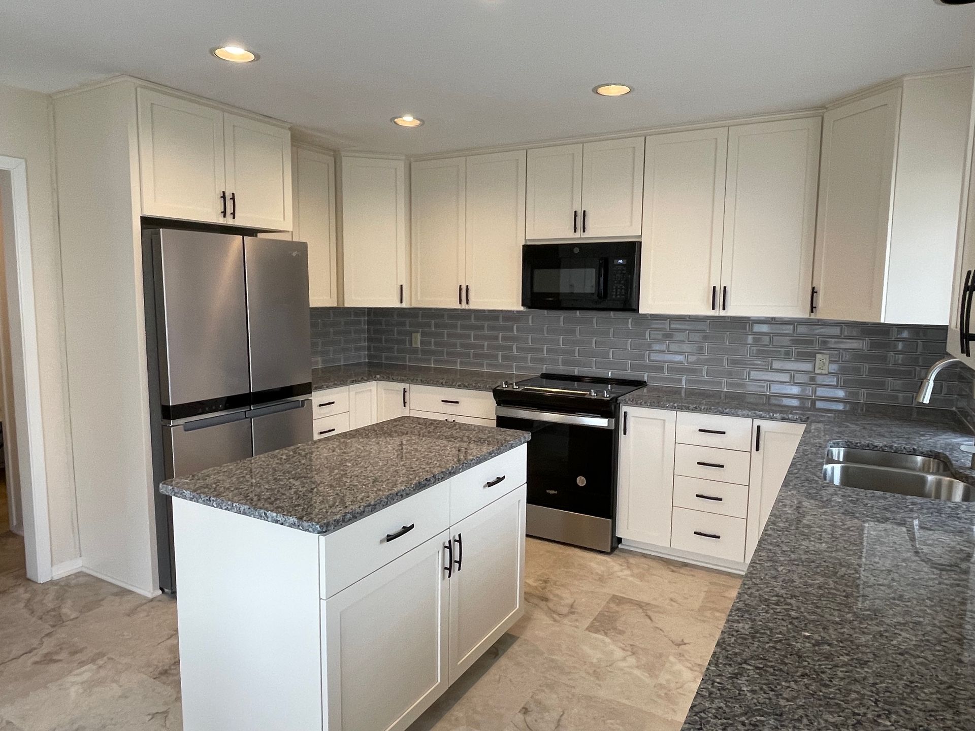 Modern kitchen with white cabinets, stainless steel appliances, granite countertops, and a gray tile backsplash.