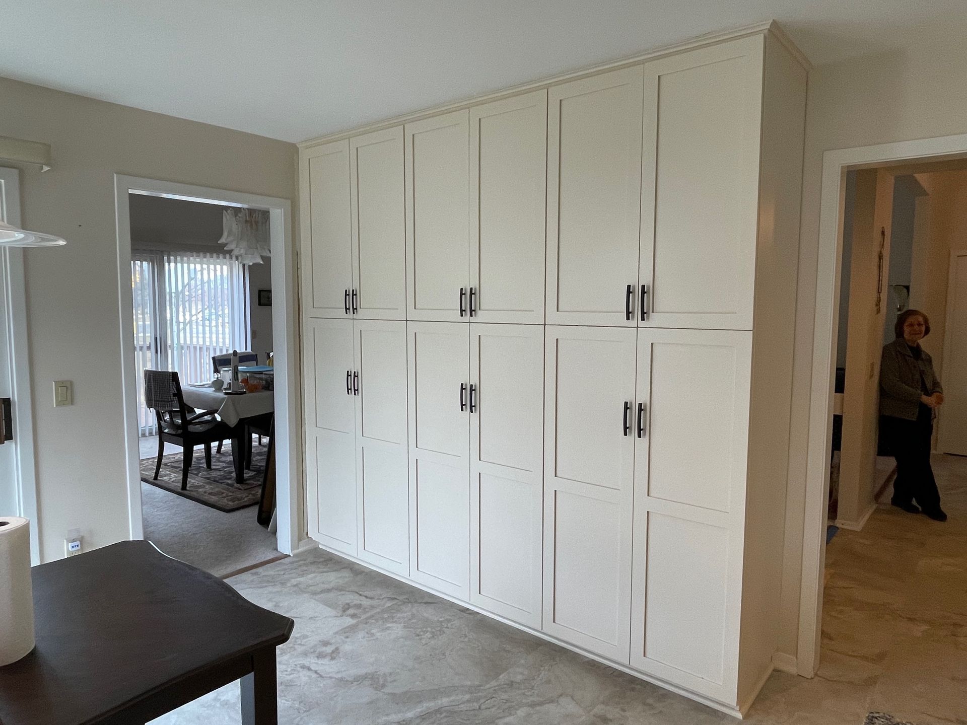 White cabinets line a wall, with black handles. Two doorways and a table are also visible.