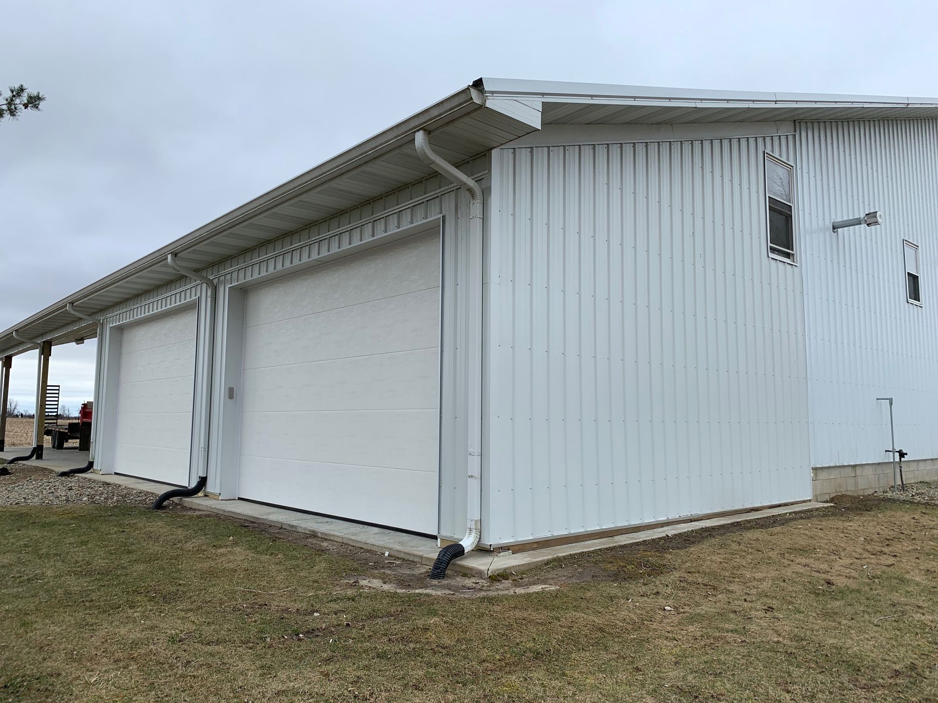 White metal building with two garage doors, gutters, and small windows on a grassy lawn.