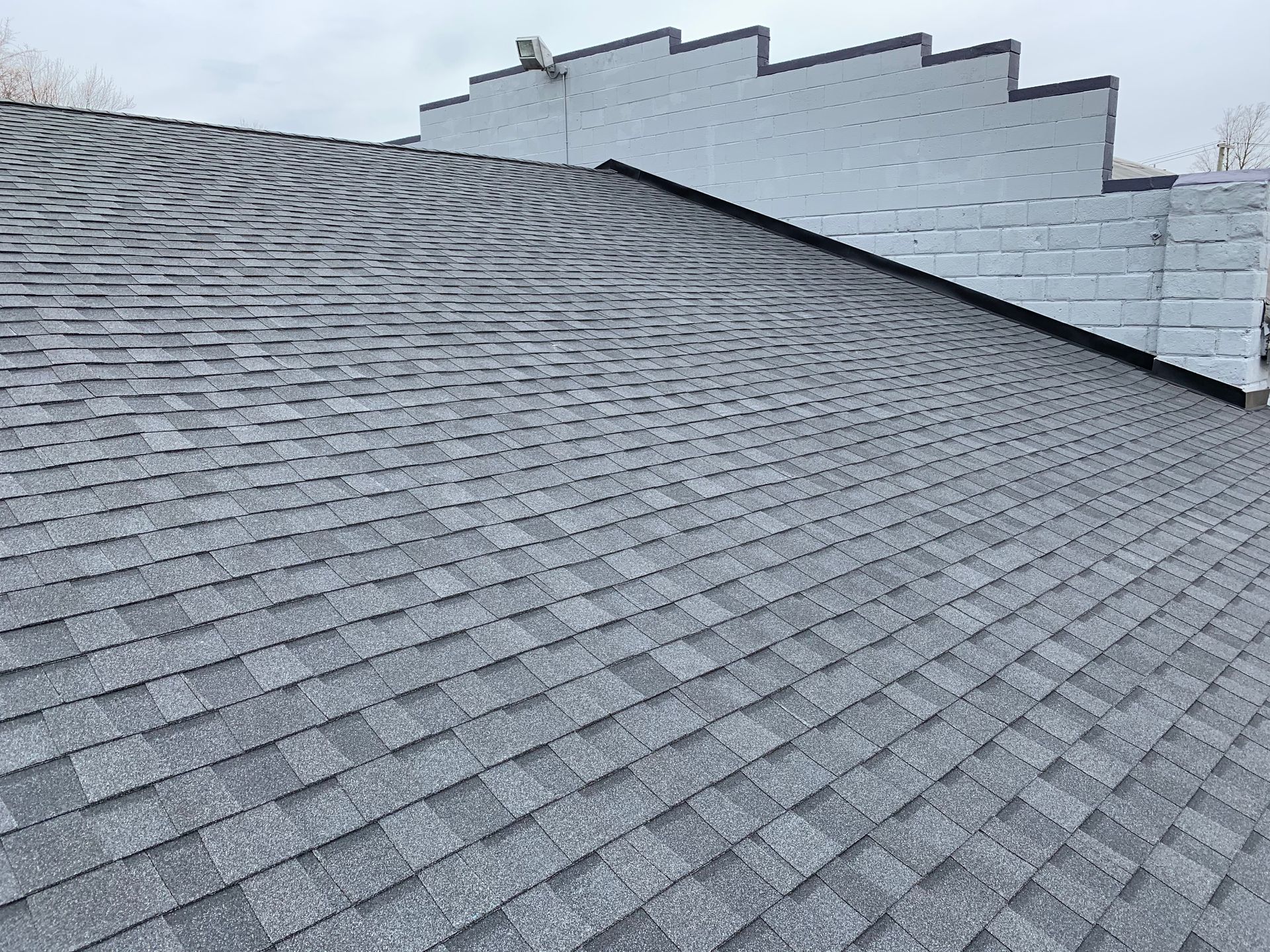 Gray asphalt shingle roof with a sawtooth-edged white wall in the background.