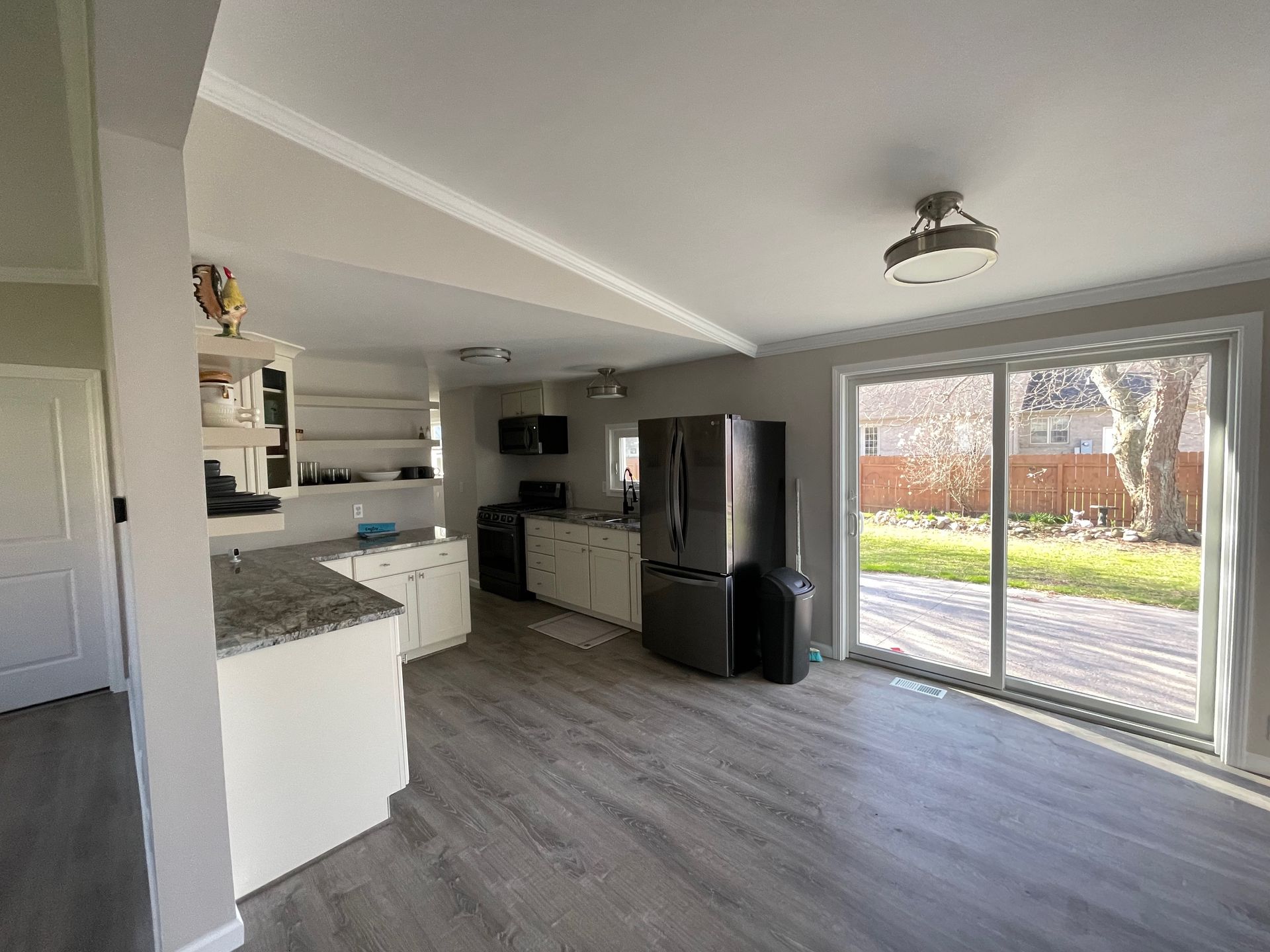 Kitchen with white cabinets, gray countertops, and stainless steel appliances; sliding glass door to backyard.