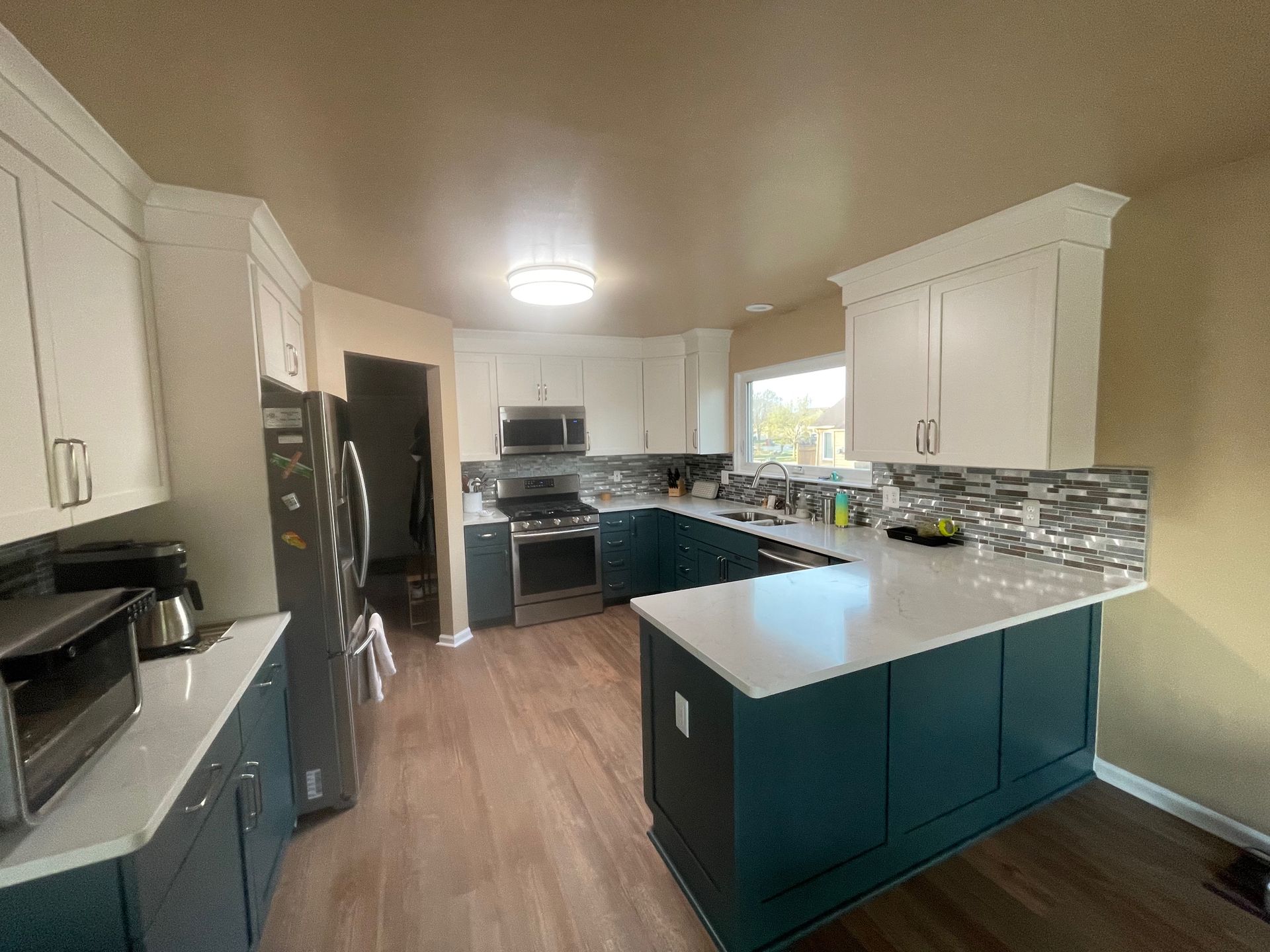 Kitchen with white upper cabinets, teal lower cabinets, white countertops, and stainless steel appliances.