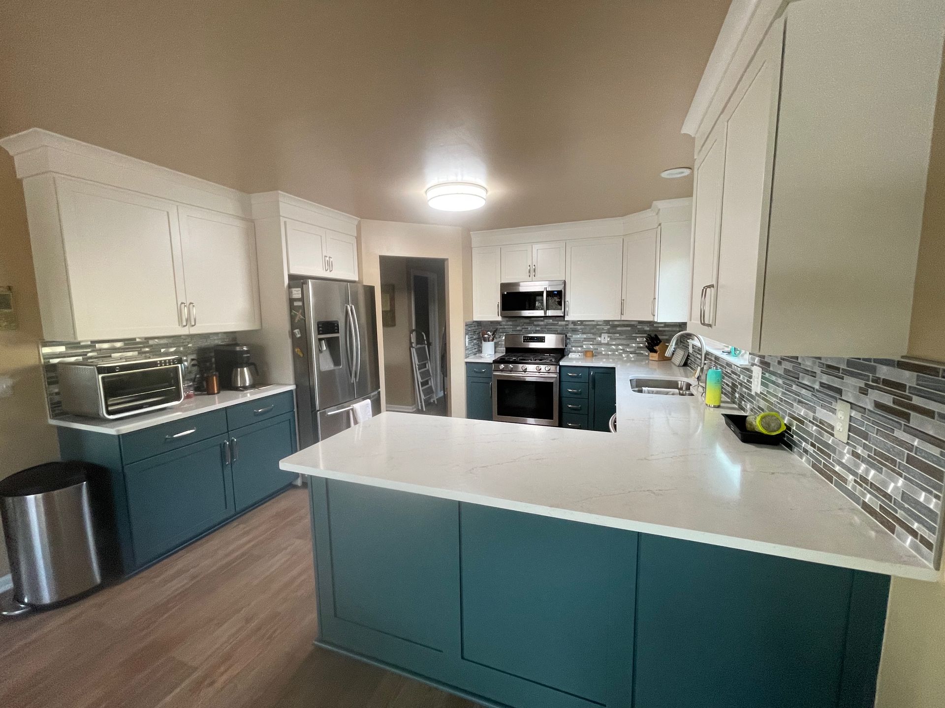 Kitchen with white upper cabinets and teal lower cabinets, stainless steel appliances, and white countertop.