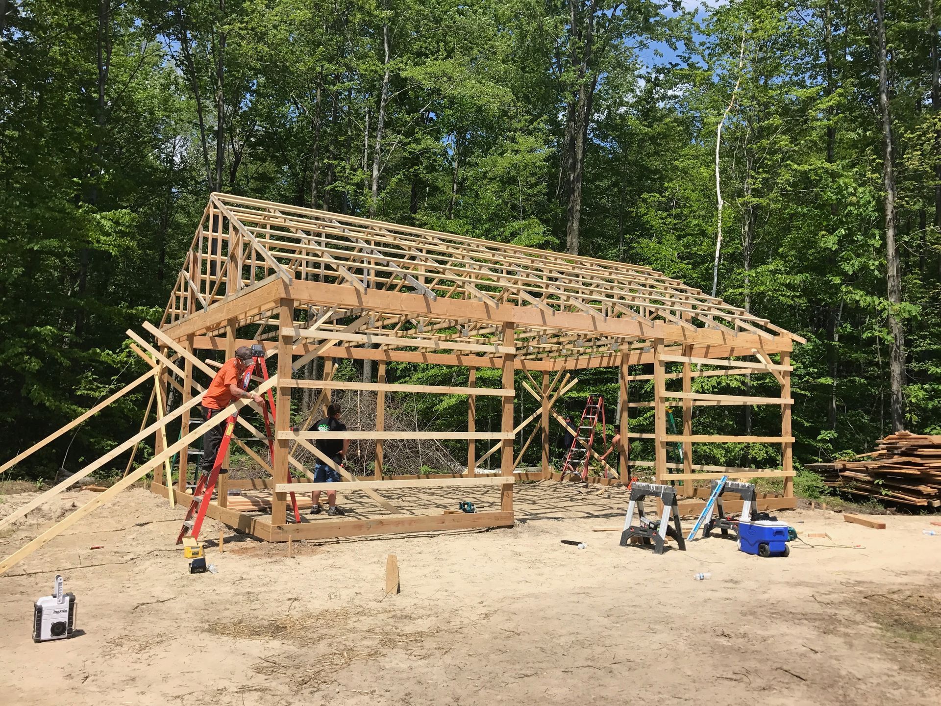 Wood frame building under construction, with workers, tools, and a wooded background.
