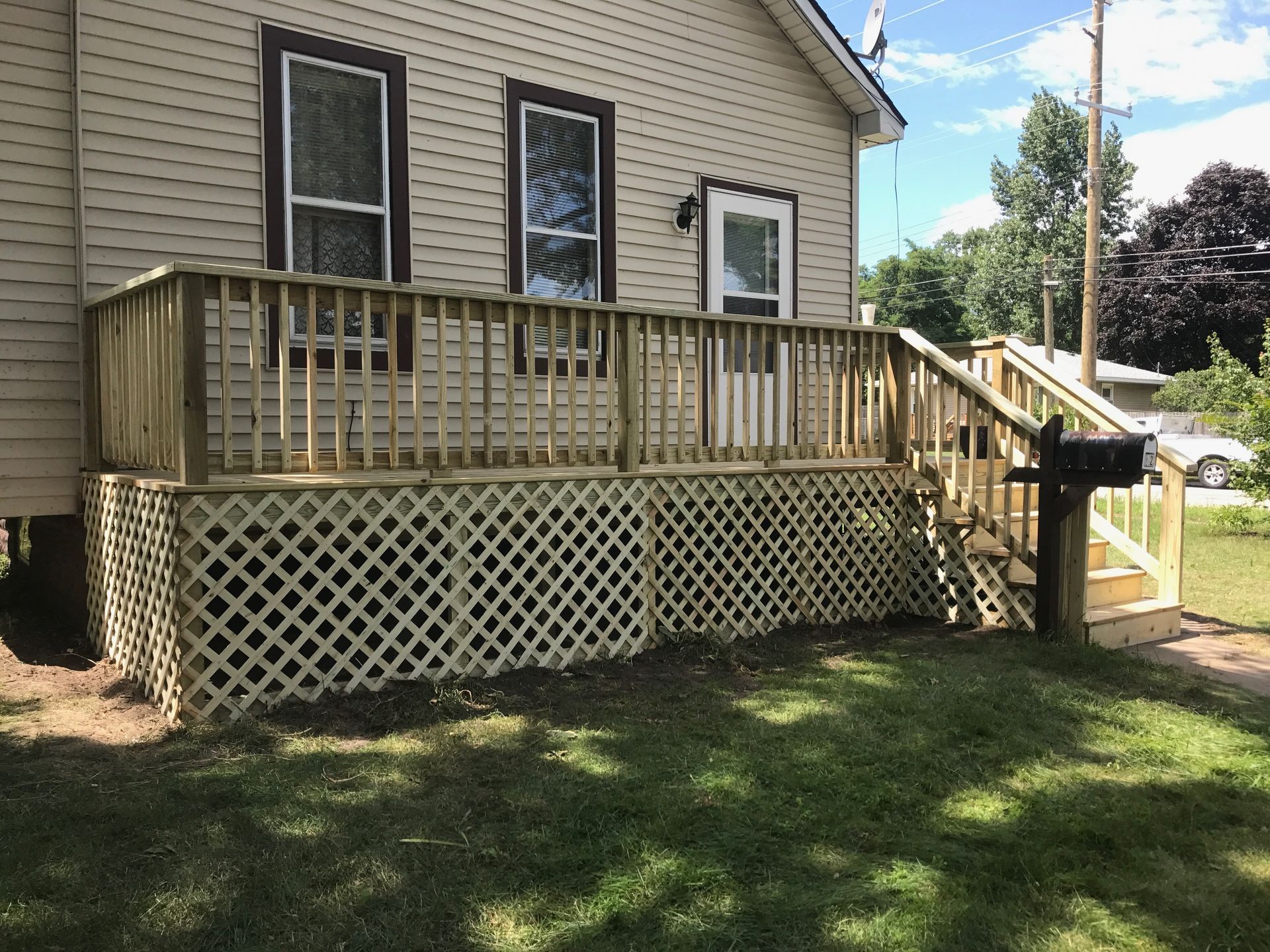 Wooden deck attached to a light-colored house with lattice skirting and a staircase in a grassy yard.