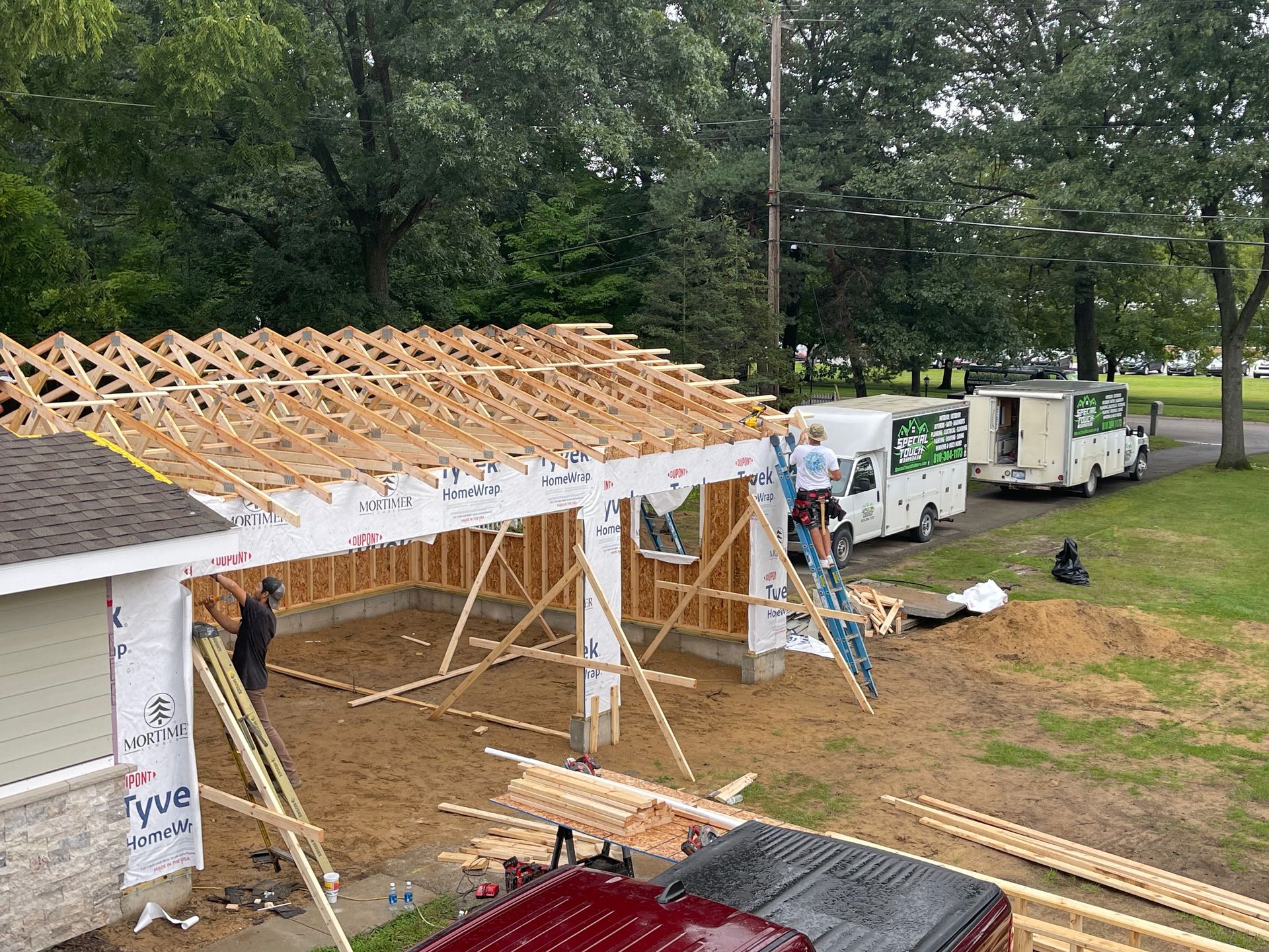 Garage under construction with workers, wood beams, and white vans parked on grass.