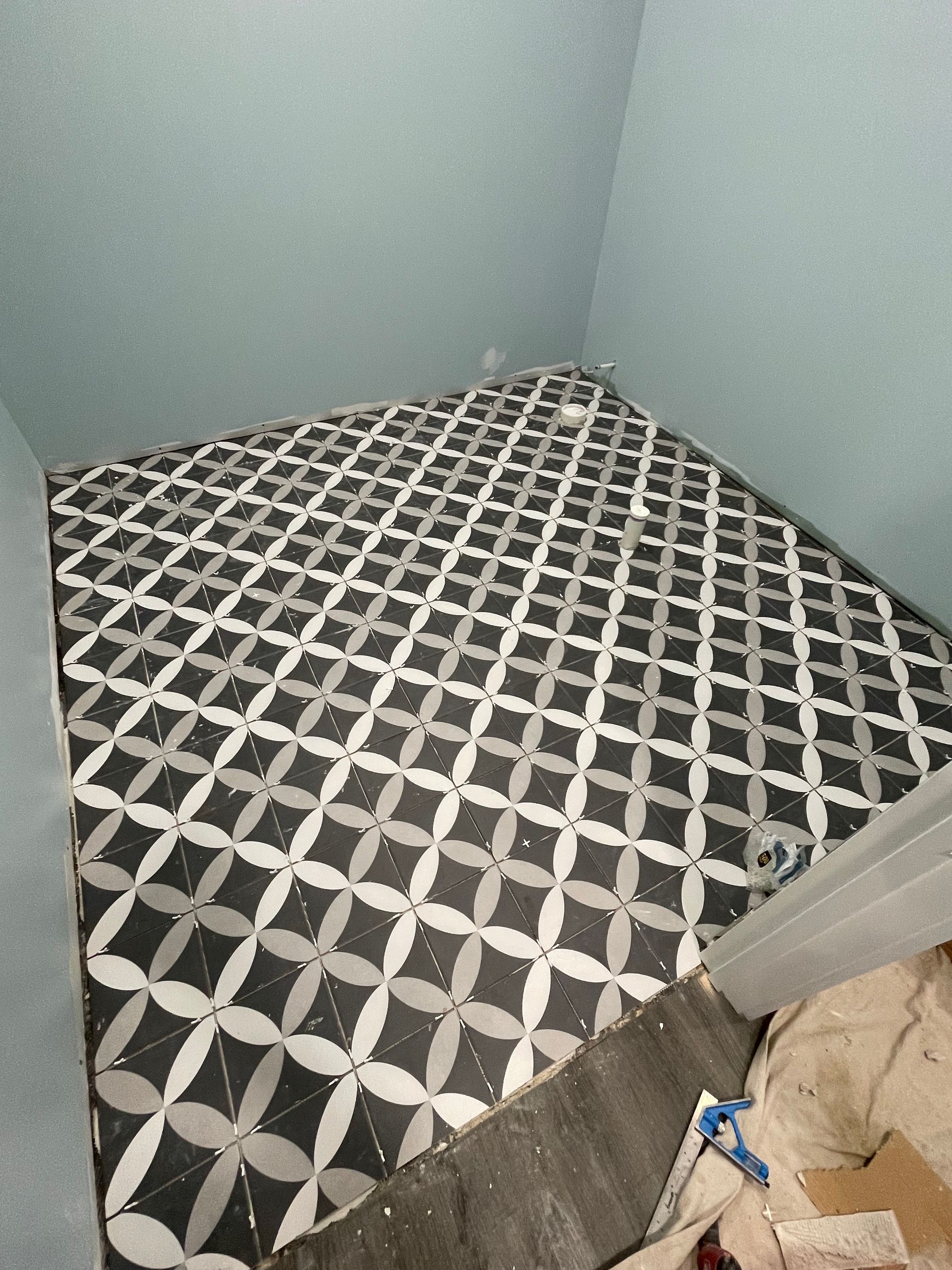 Black, white, and gray patterned tiles on a floor inside a corner. Blue wall above.