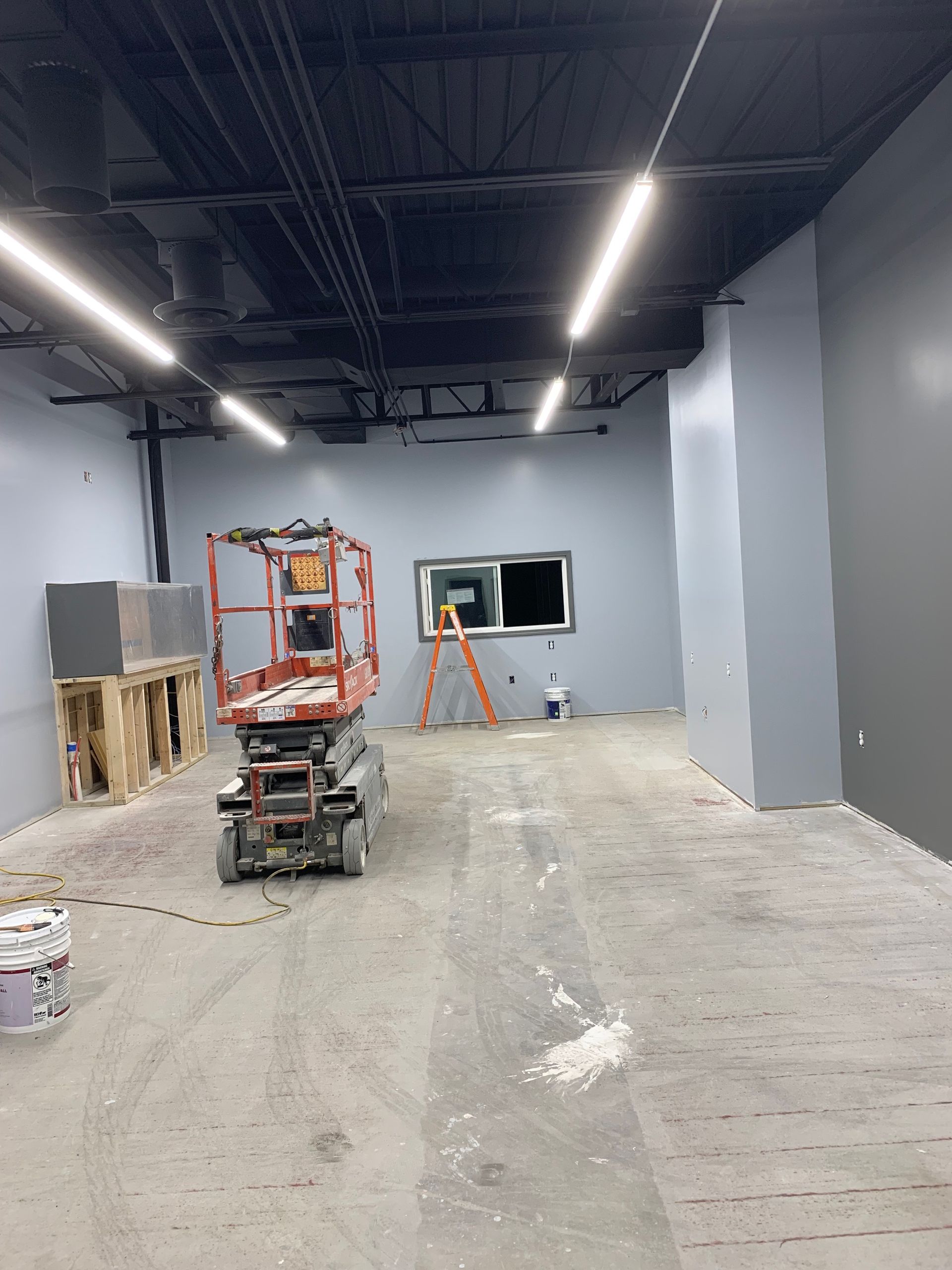 An interior of a room under construction with a scissor lift and a window. Walls are painted gray.