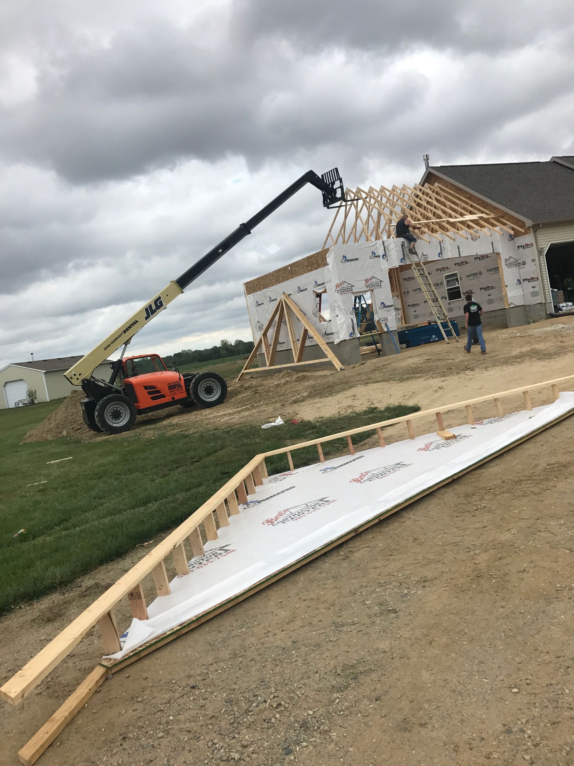 Construction site: orange lift, new house framing, worker, overcast sky.