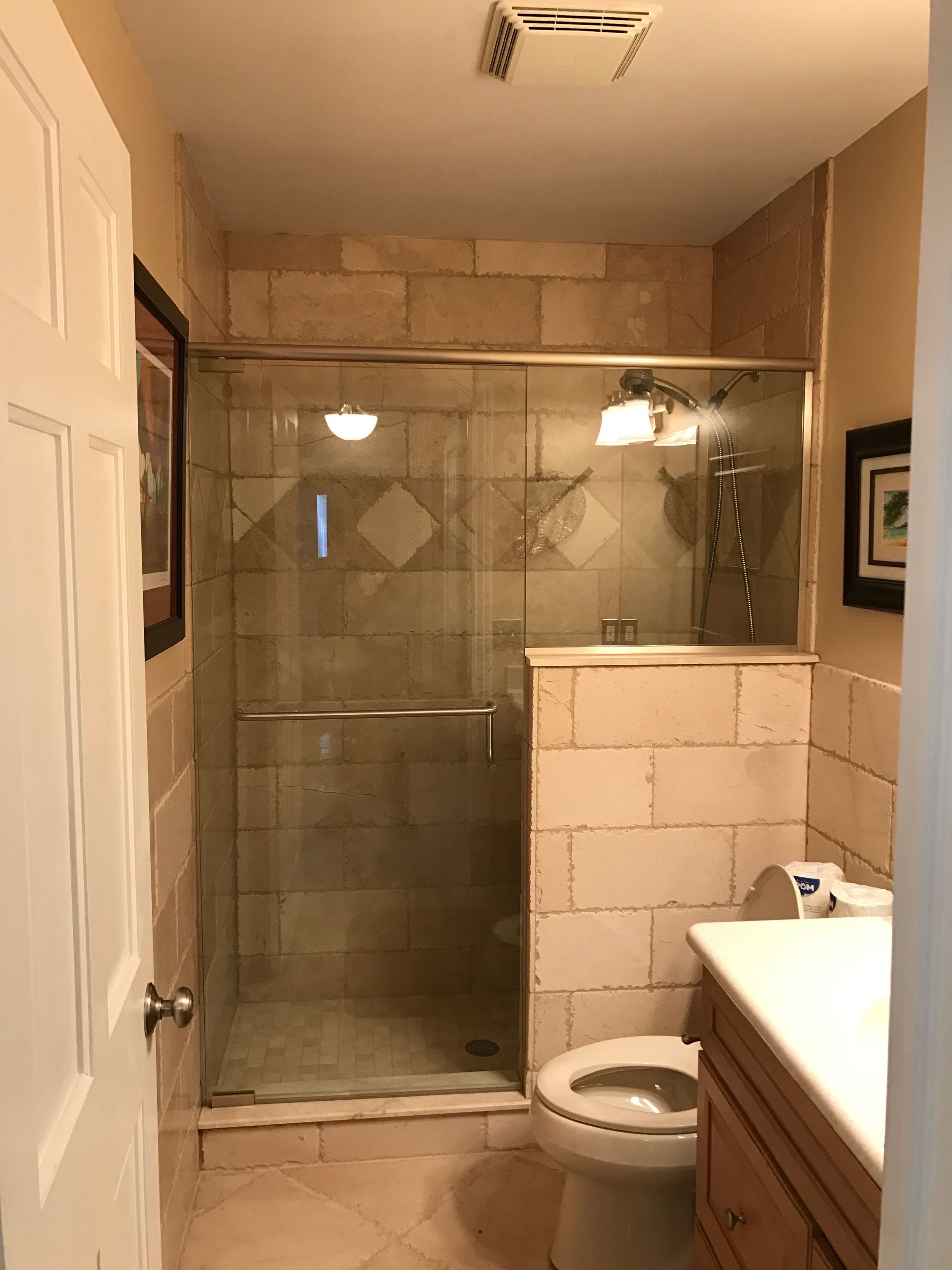Bathroom with a tiled shower, toilet, and vanity. Beige and light-colored.