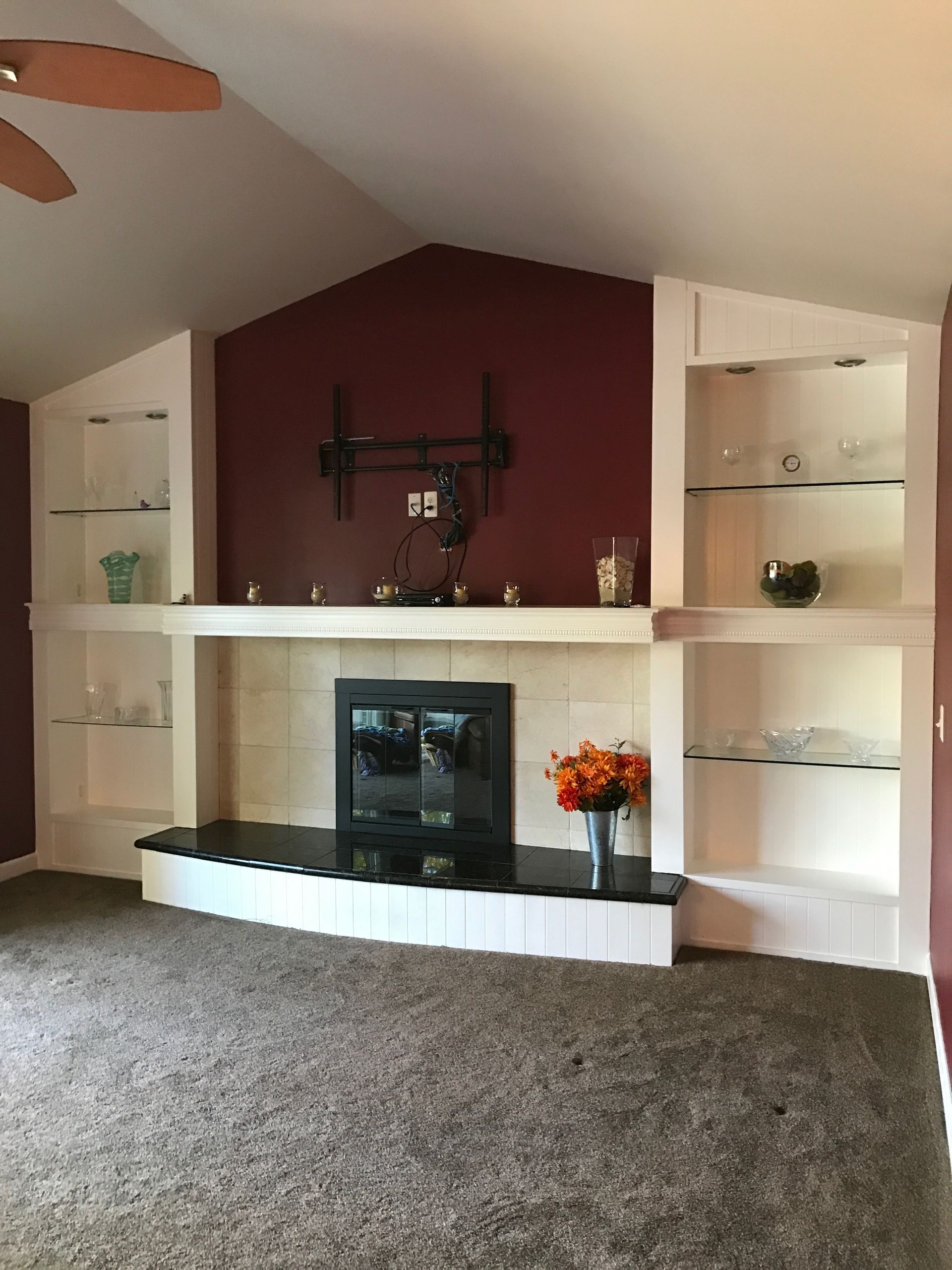 Fireplace with built-in shelves. Red accent wall, TV mount, glass shelves, and orange flowers.