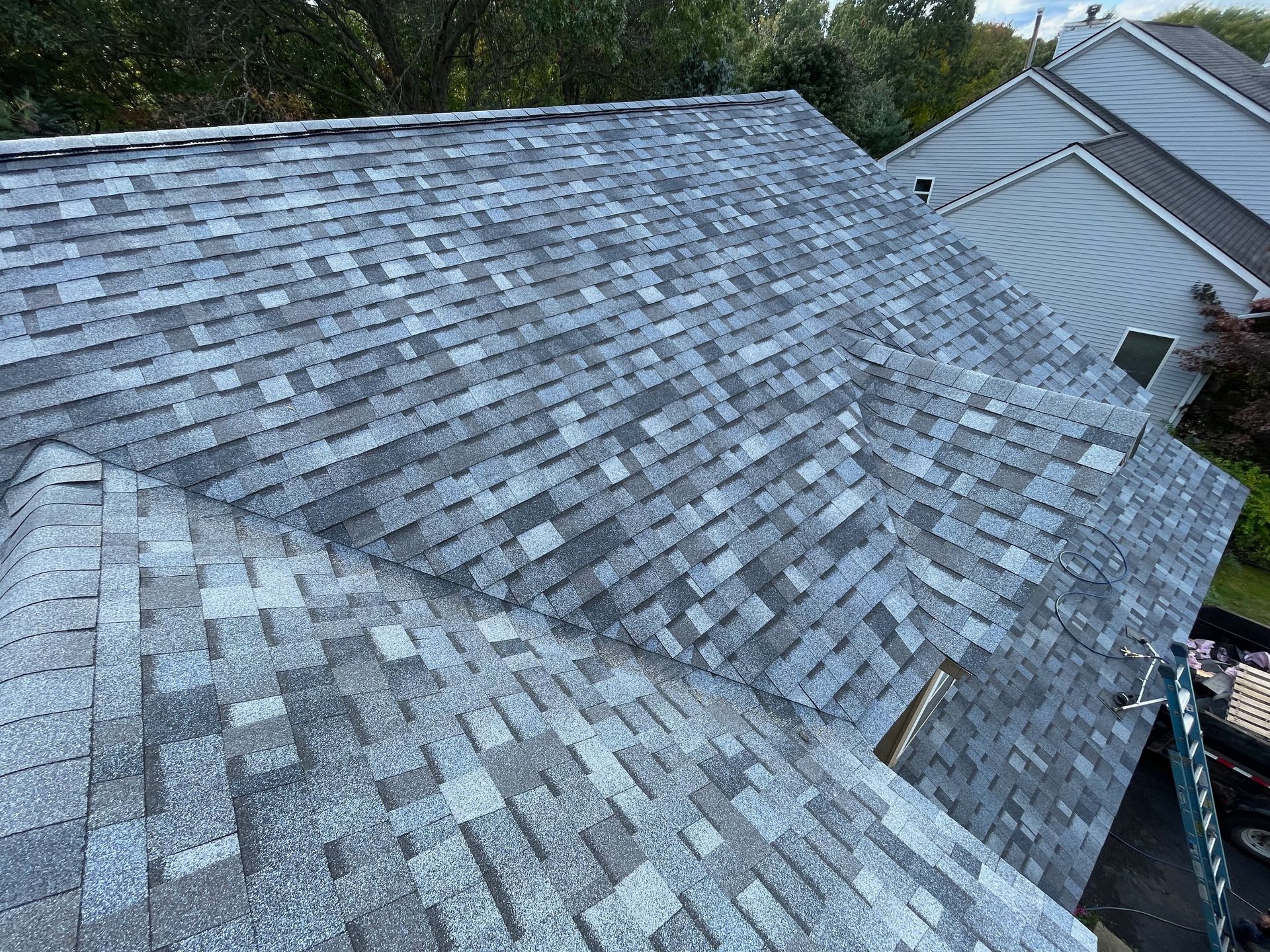 Grey asphalt shingle roof, angled view, overcast sky. Some dark patches present.