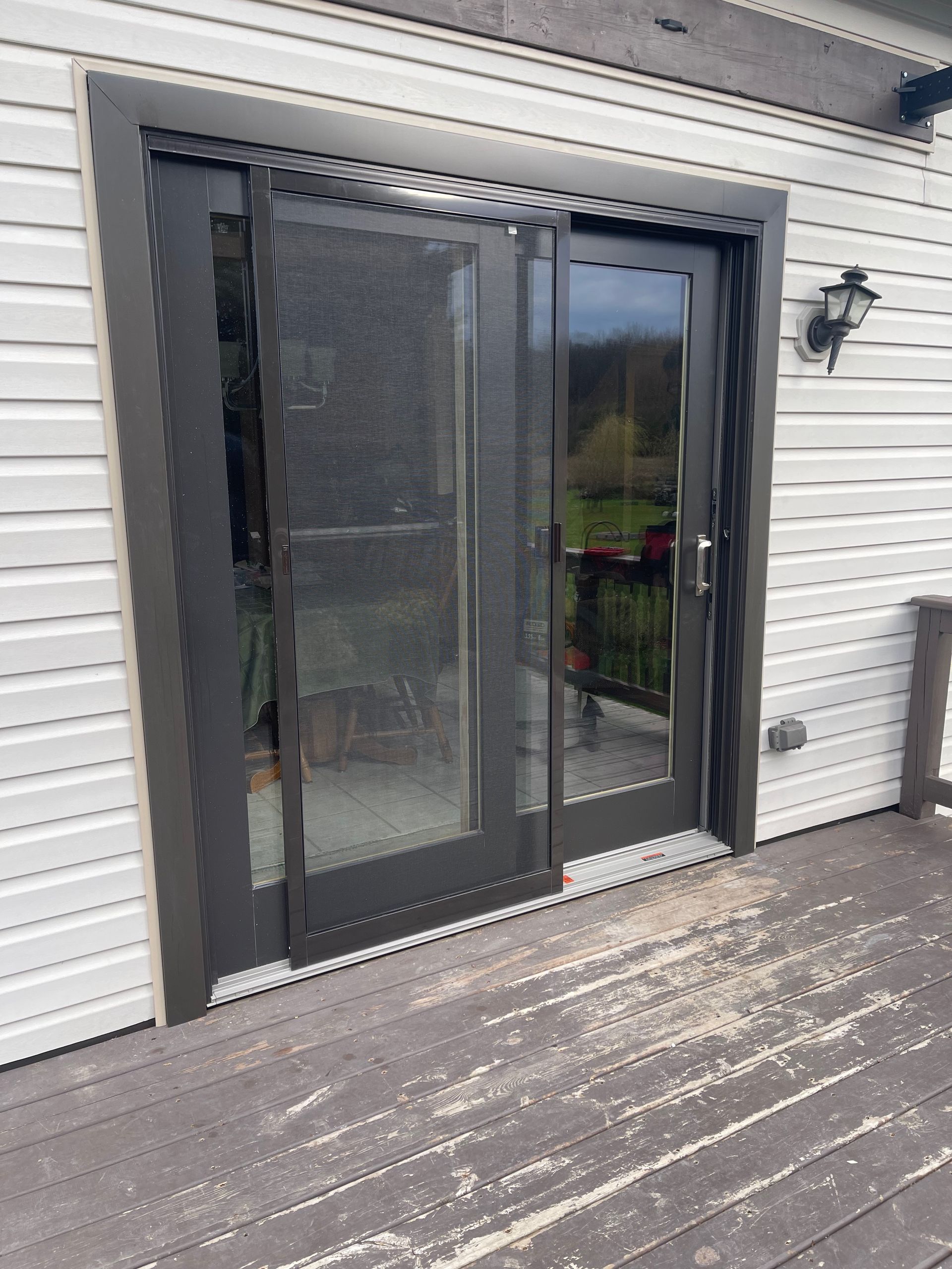 Black framed glass doors on a weathered wooden deck. Dark gray trim against white siding.