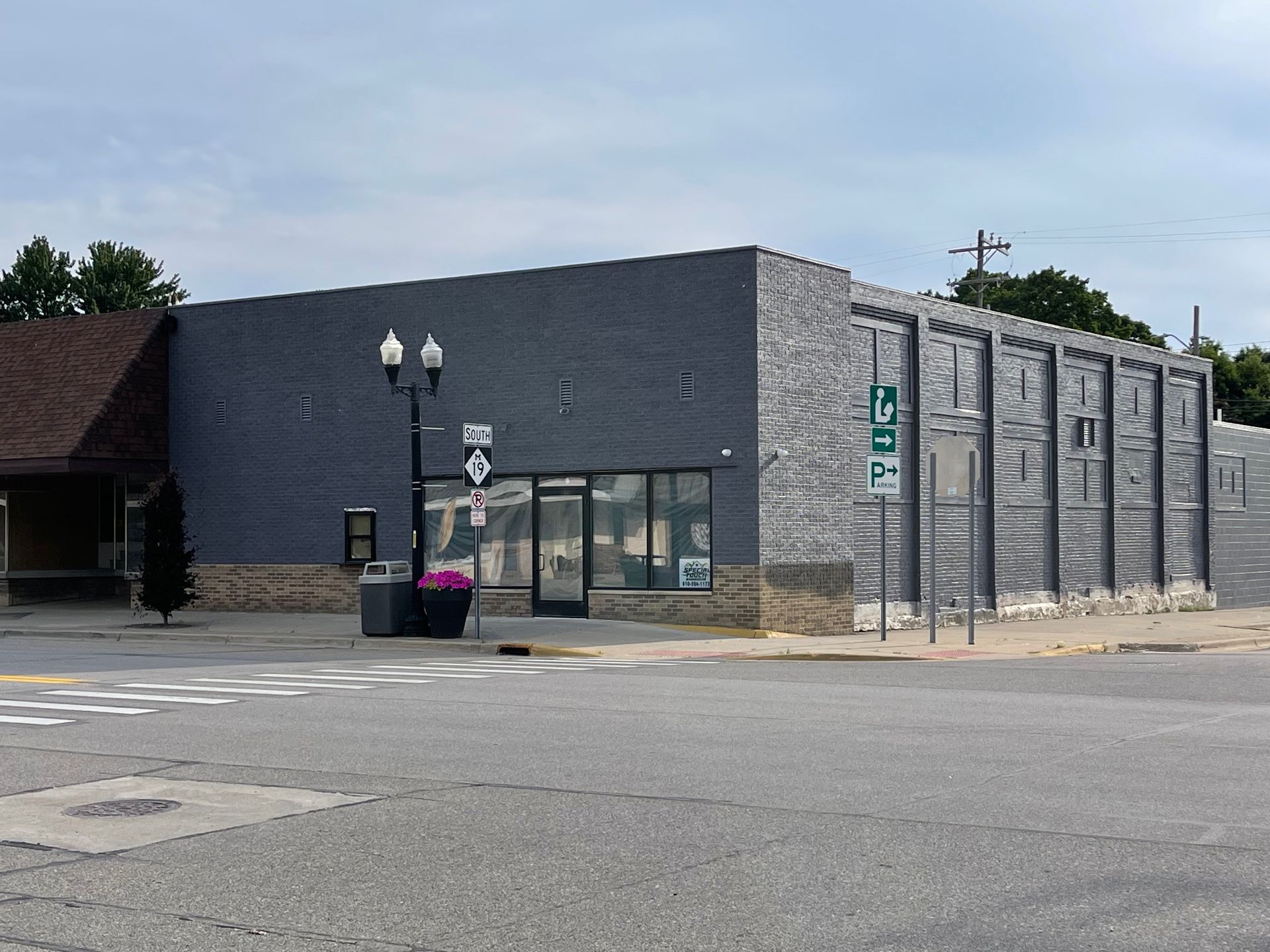 A gray building with a glass storefront, street lamps, and a crosswalk on a sunny day.