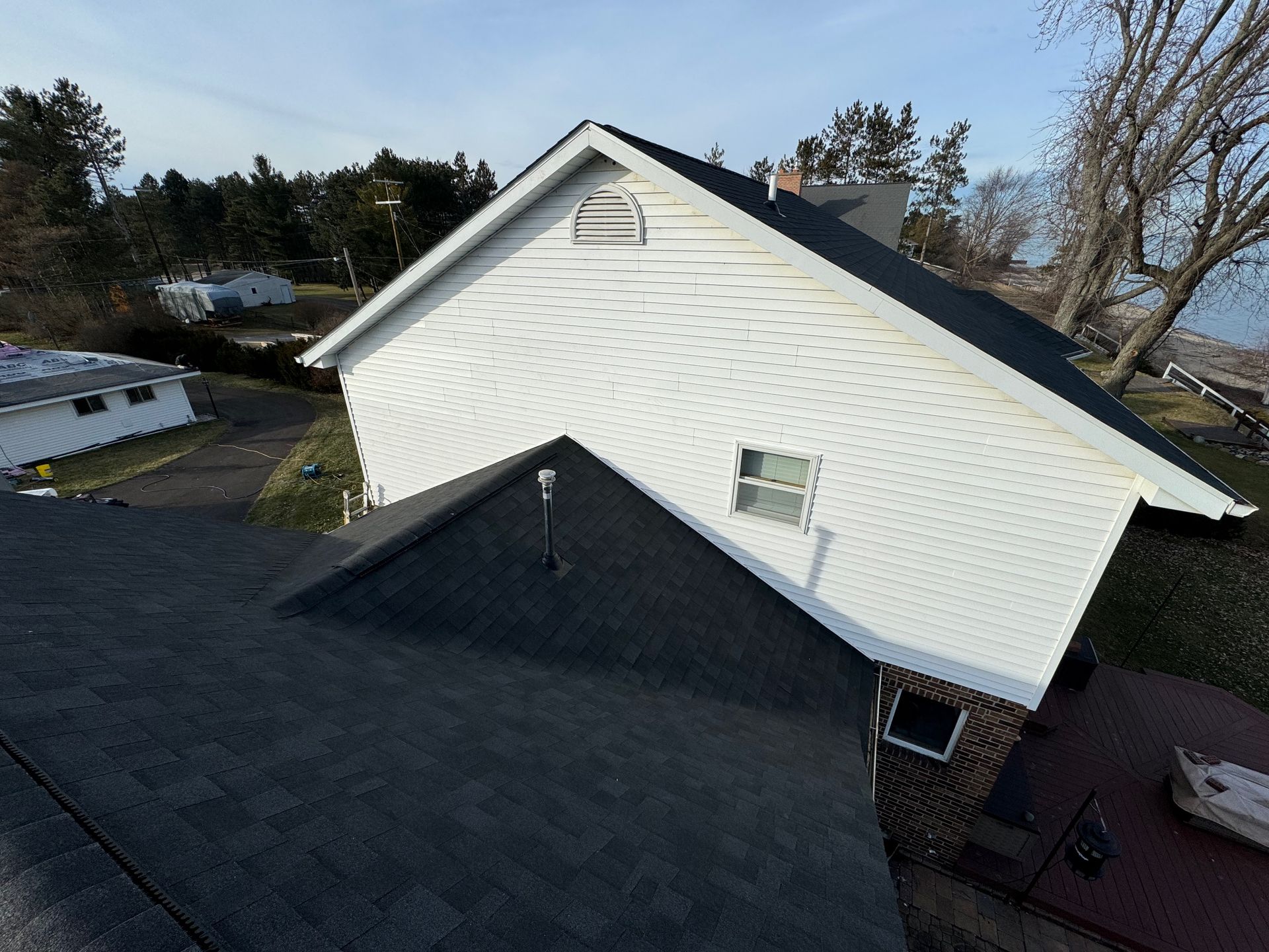 View of a house with white siding and a dark gray shingled roof, set next to a body of water.