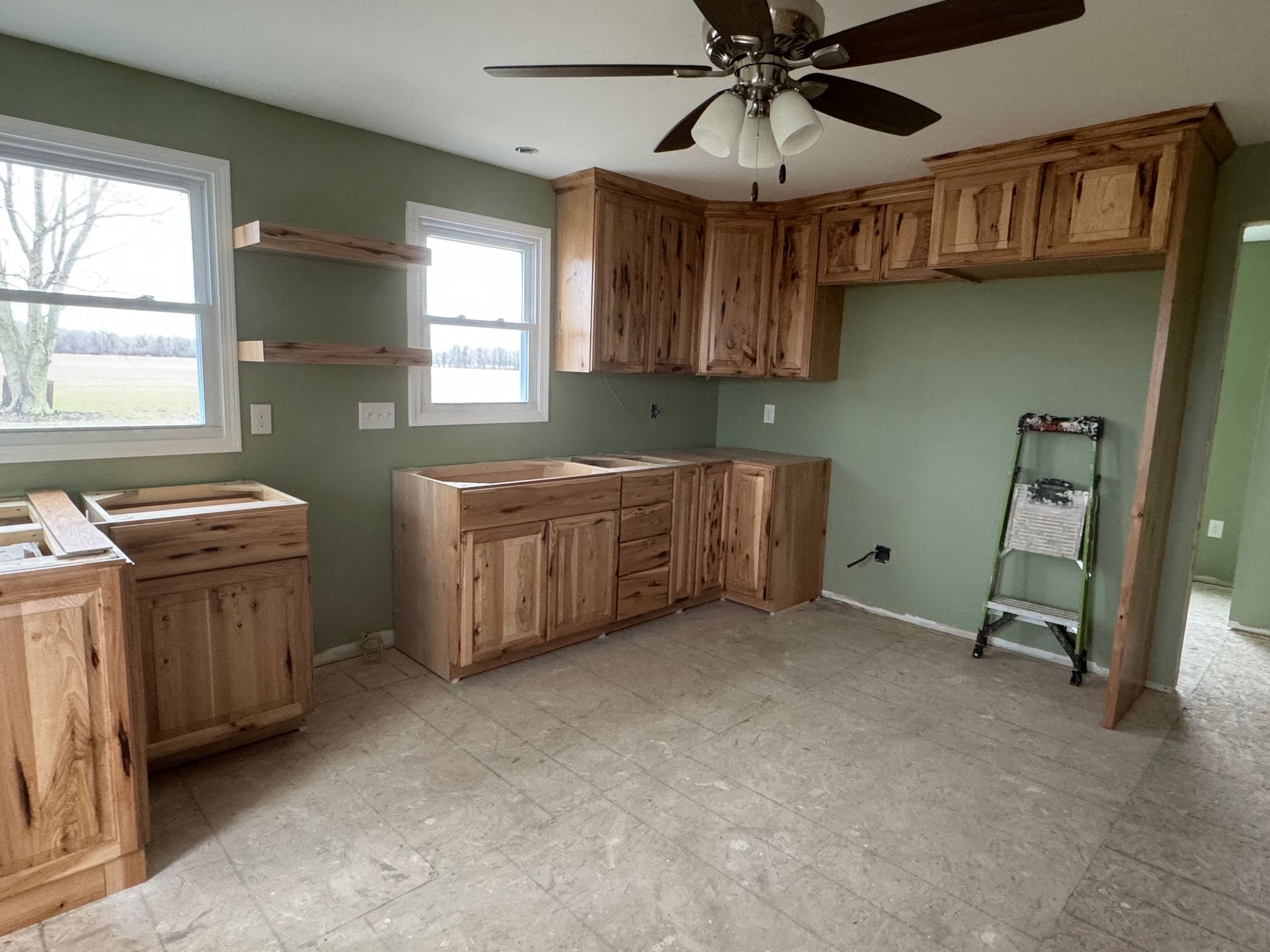 Kitchen with light wood cabinets, green walls, and a ceiling fan, under construction.