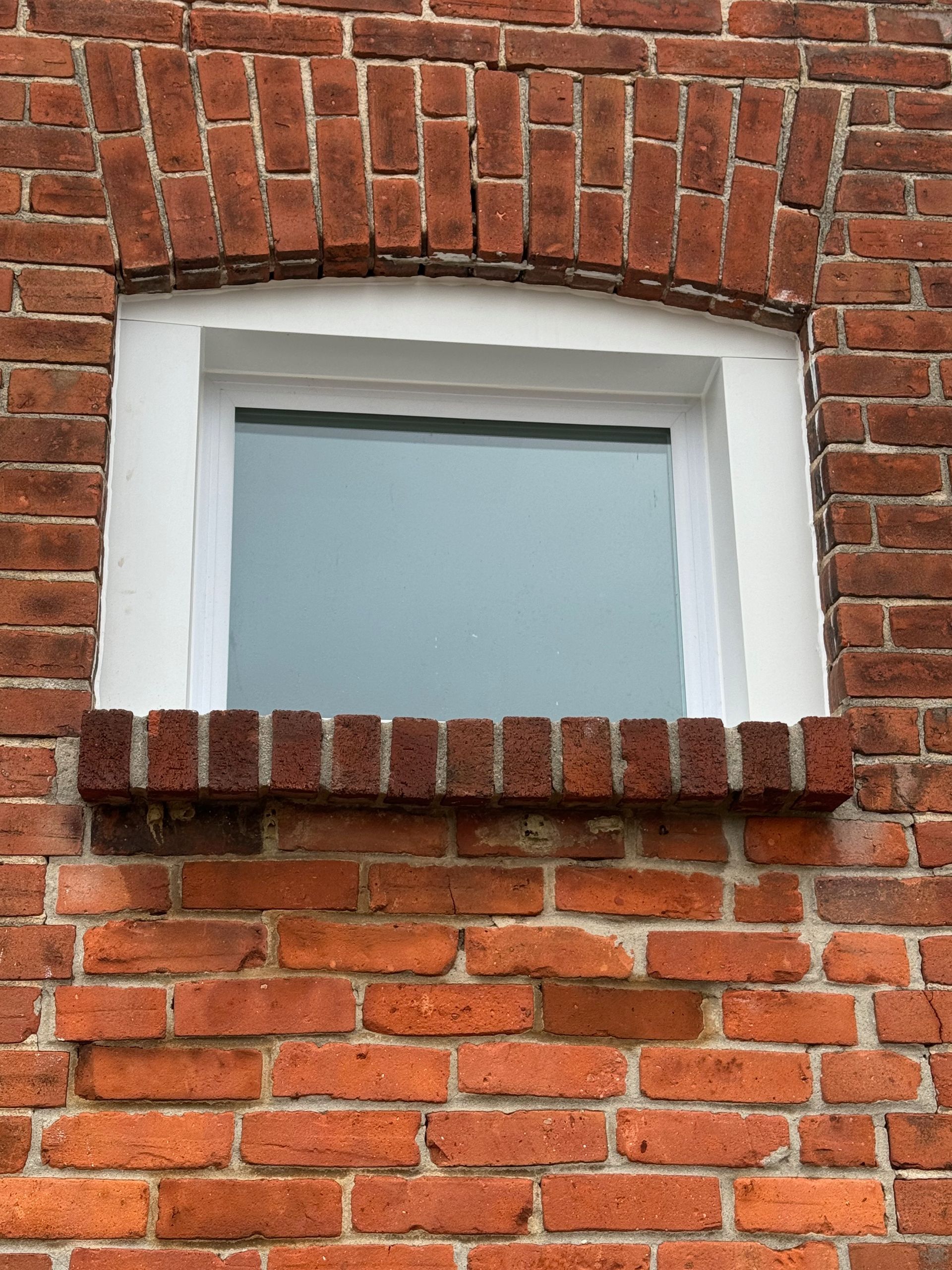 Brick building with a white-framed window. Arched brickwork above the window, brick sill below.
