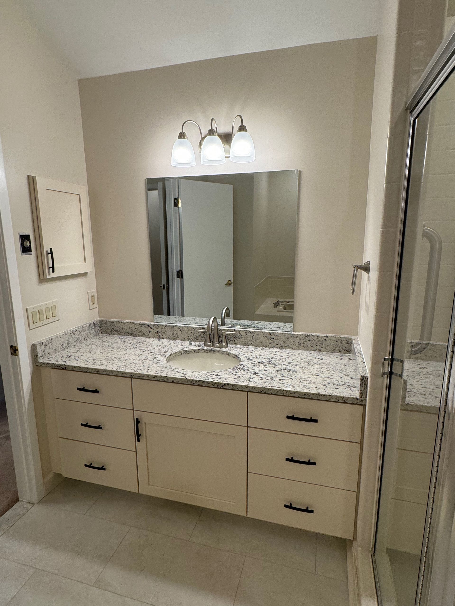 Bathroom vanity with marble countertop, beige cabinets, rectangular mirror, and three-light fixture.