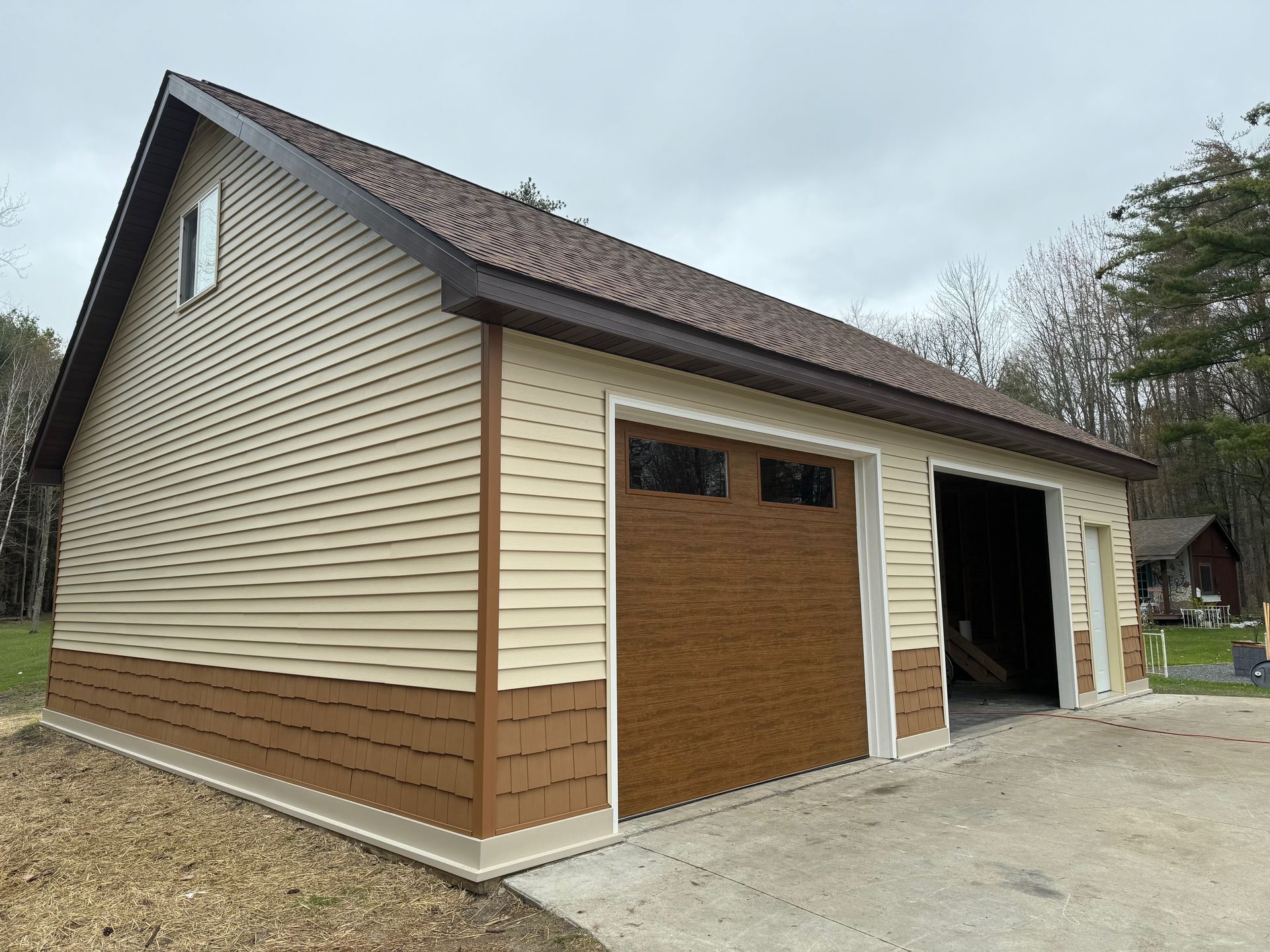 Tan and brown two-car garage with a brown roof and doors, standing on a concrete foundation under a cloudy sky.