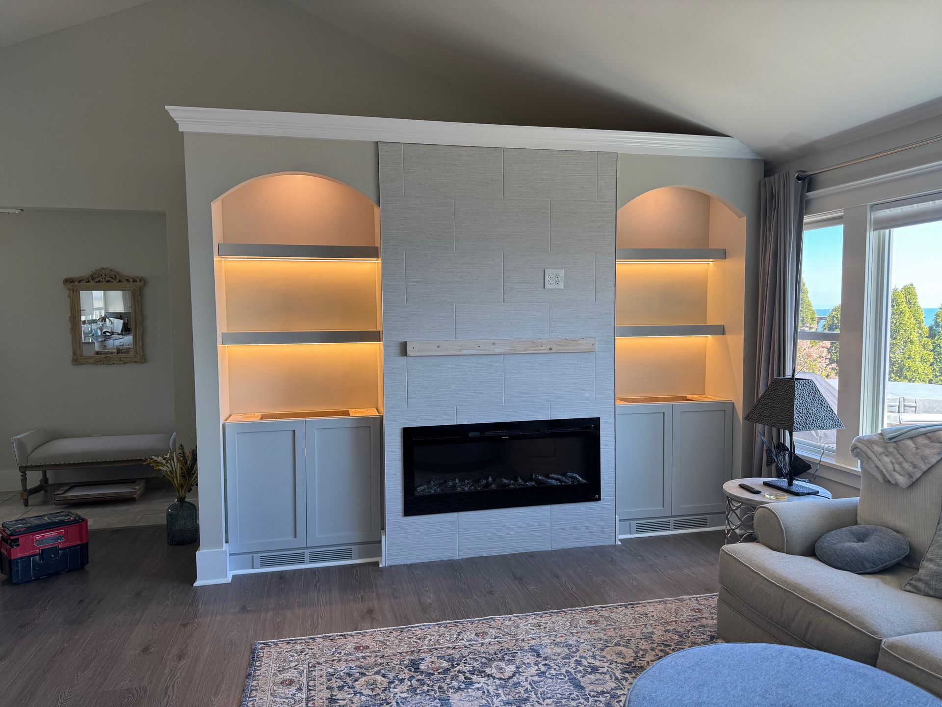 Built-in gray bookcase with fireplace, arched shelves with lighting, and cabinet storage.