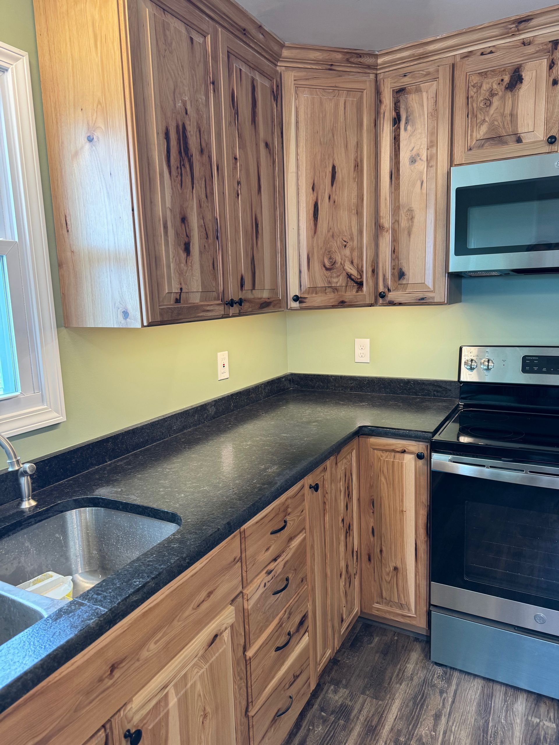 Kitchen with light wood cabinets, dark countertops, stainless steel appliances, and sage green walls.