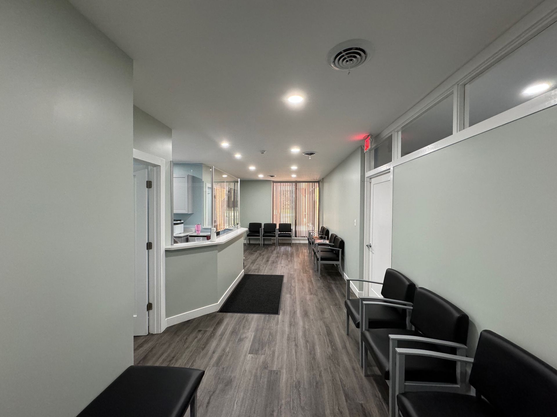 A medical office waiting room with chairs, reception desk, and frosted windows.