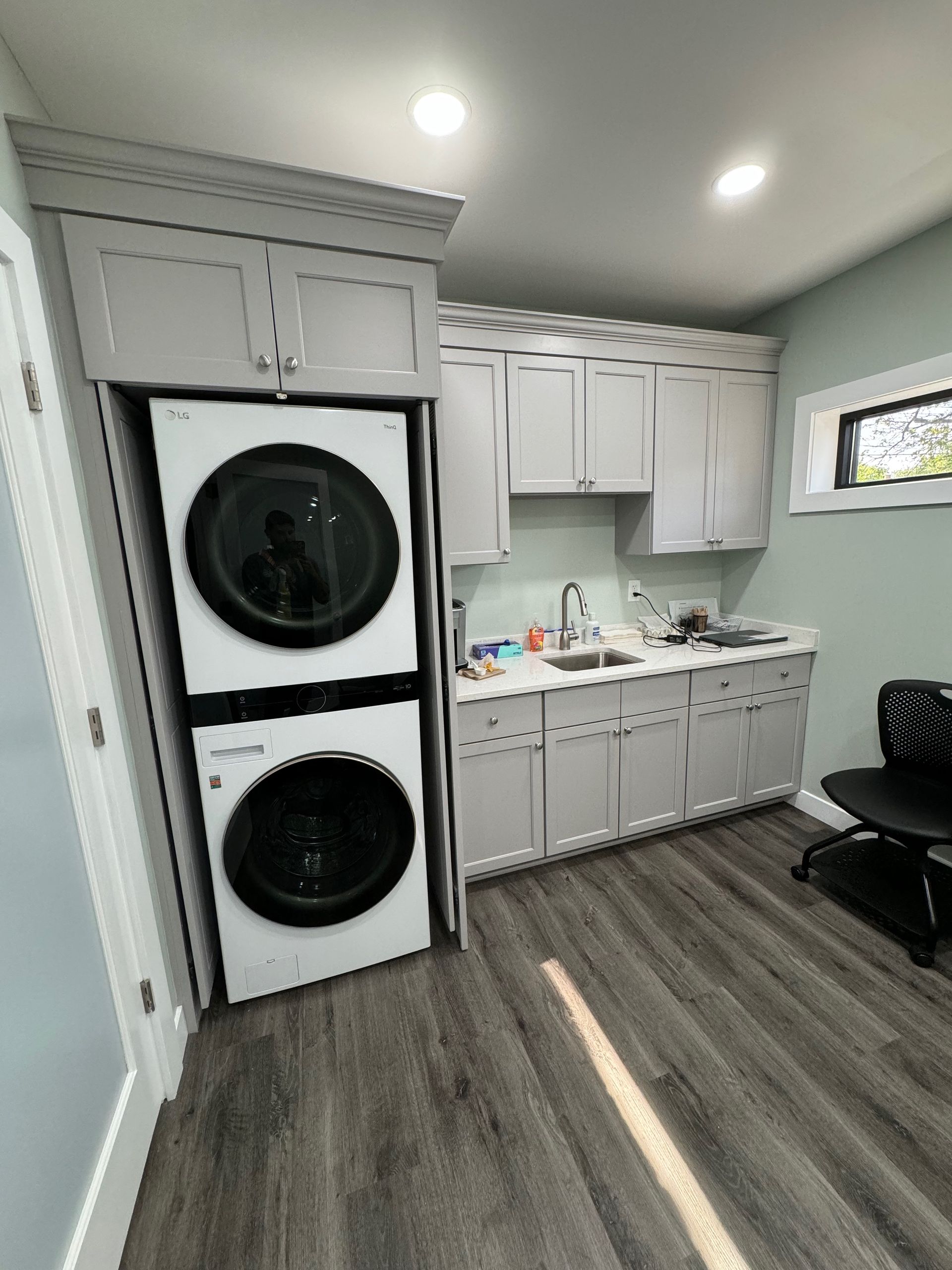 Laundry room with stacked washer/dryer, sink, cabinets, and a window.