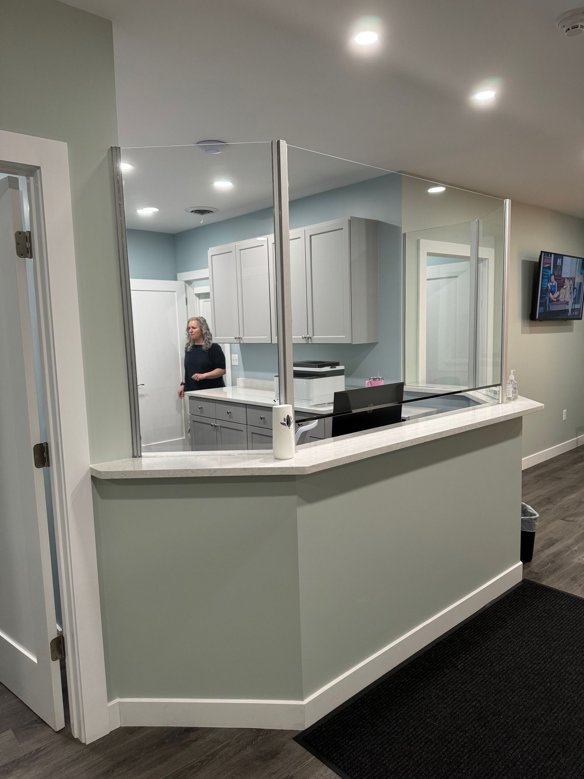 Reception desk with protective glass, light blue walls, woman standing inside.