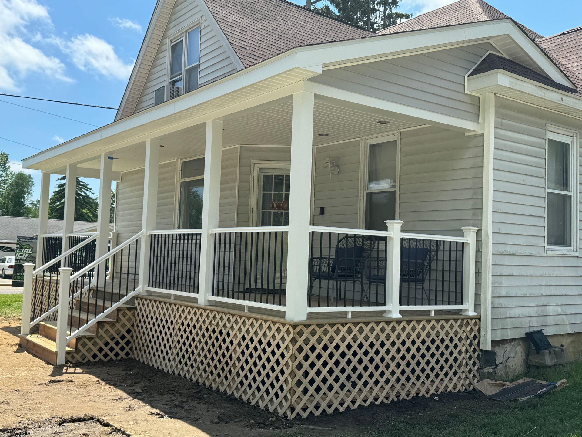 A house with a white porch. White railing and lattice skirt. Brown roof.