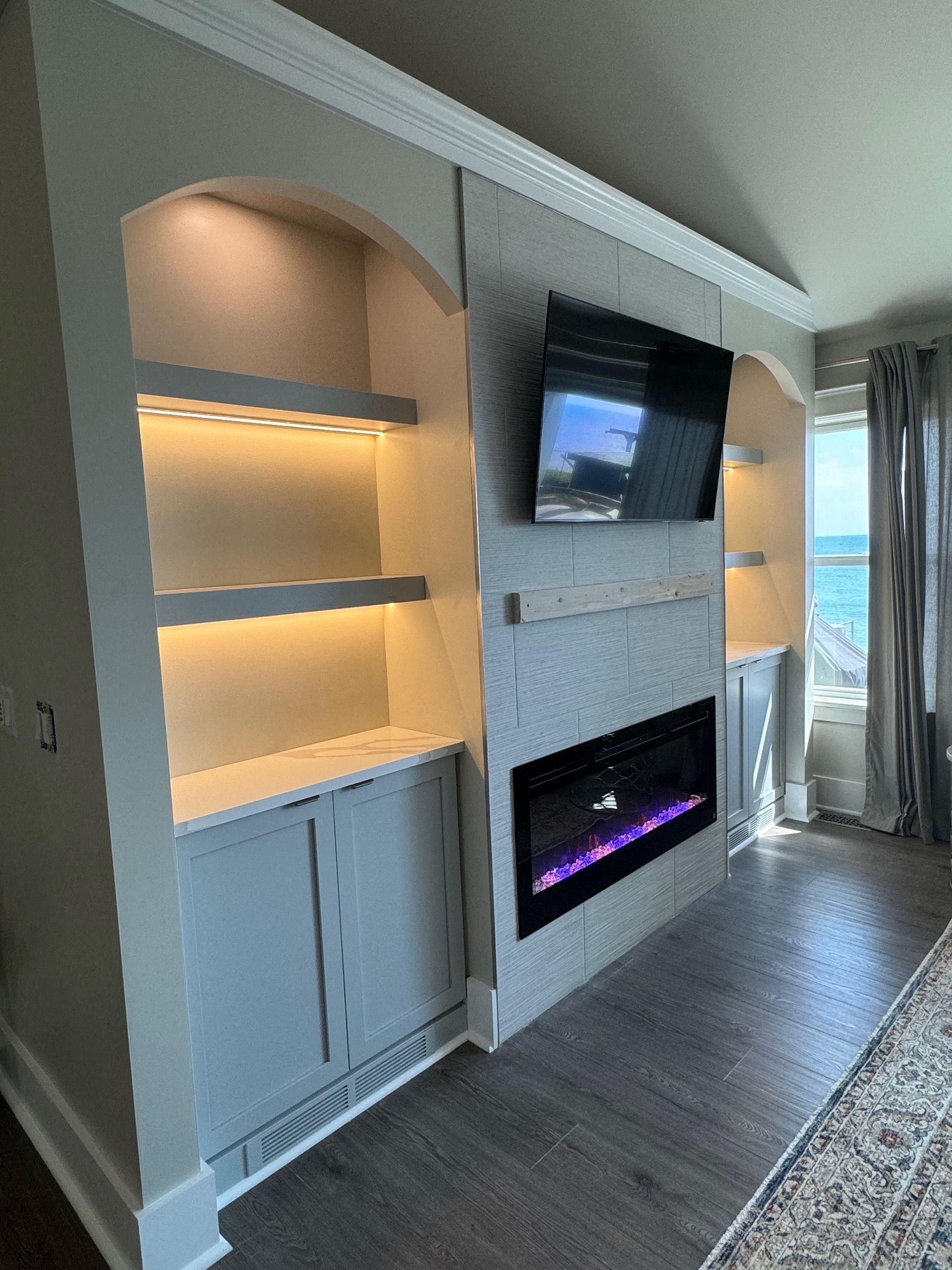 Built-in bookshelves and fireplace with a mounted TV, painted gray. Bookshelves are lit, modern setting.