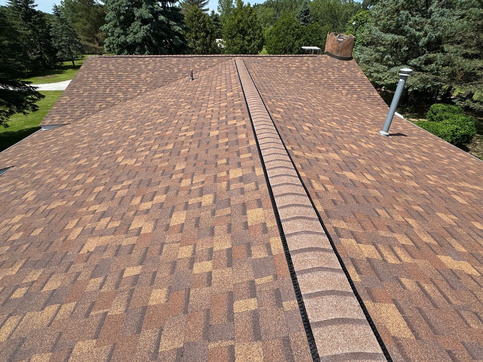 Brown asphalt shingle roof with a central ridge, chimney, and vent pipe.