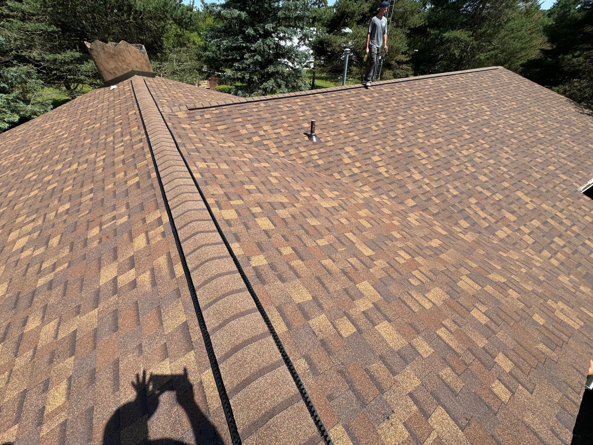 Brown asphalt shingle roof with a person standing on it, sunny outdoors.