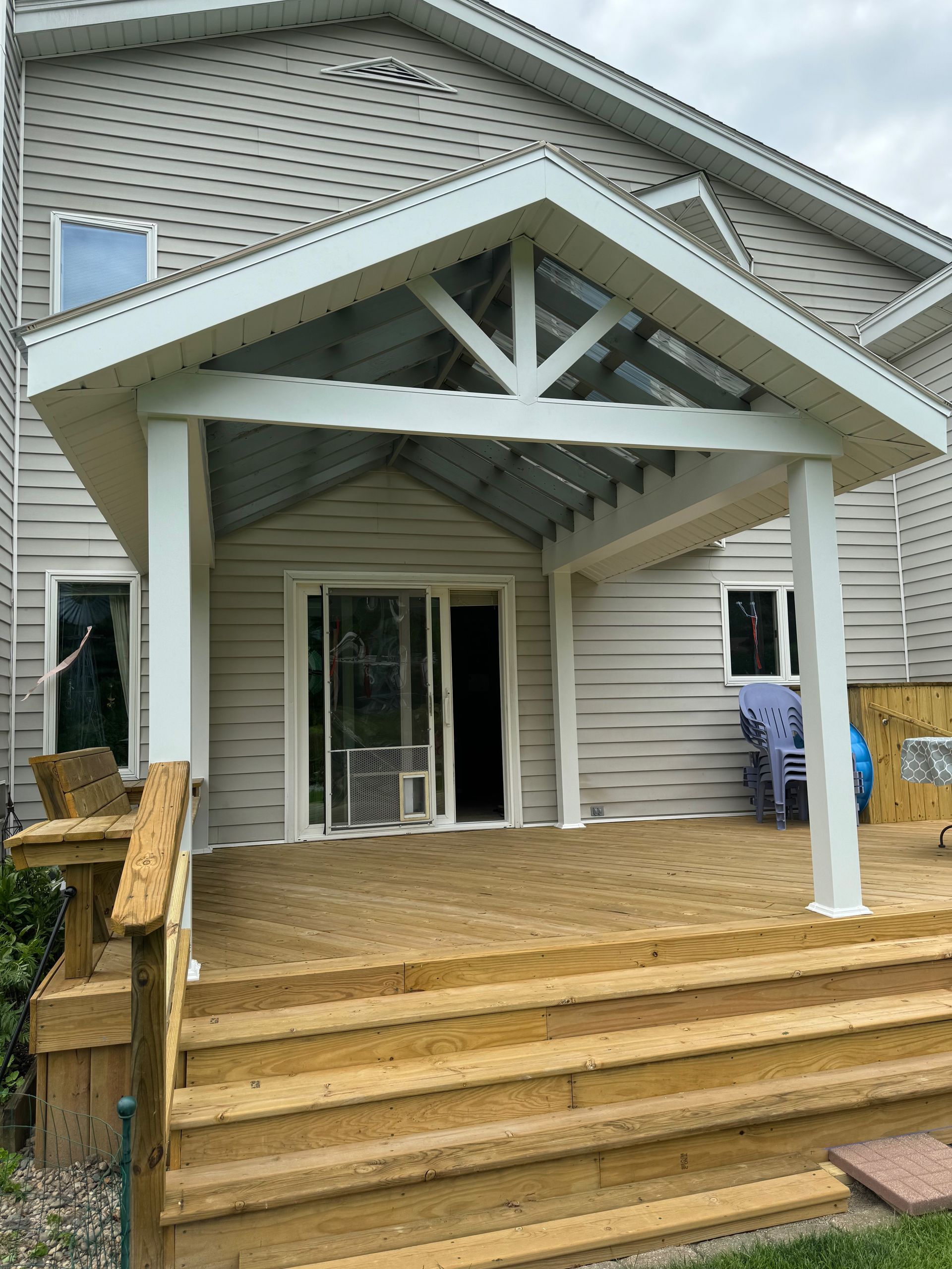 Covered deck attached to a two-story house with a white trim and sliding glass doors.