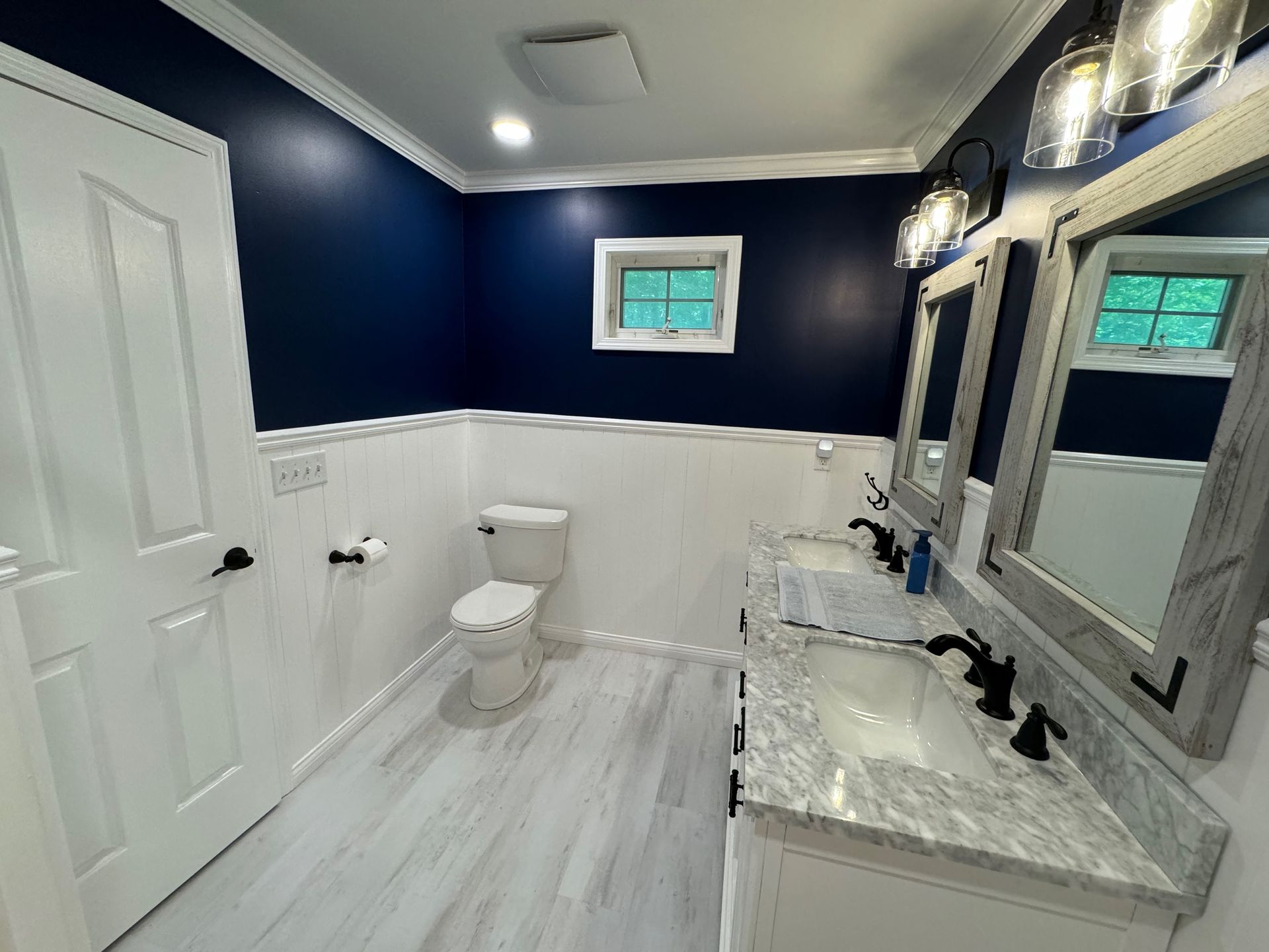 Bathroom with blue and white walls, dual sinks, toilet, and a small window.