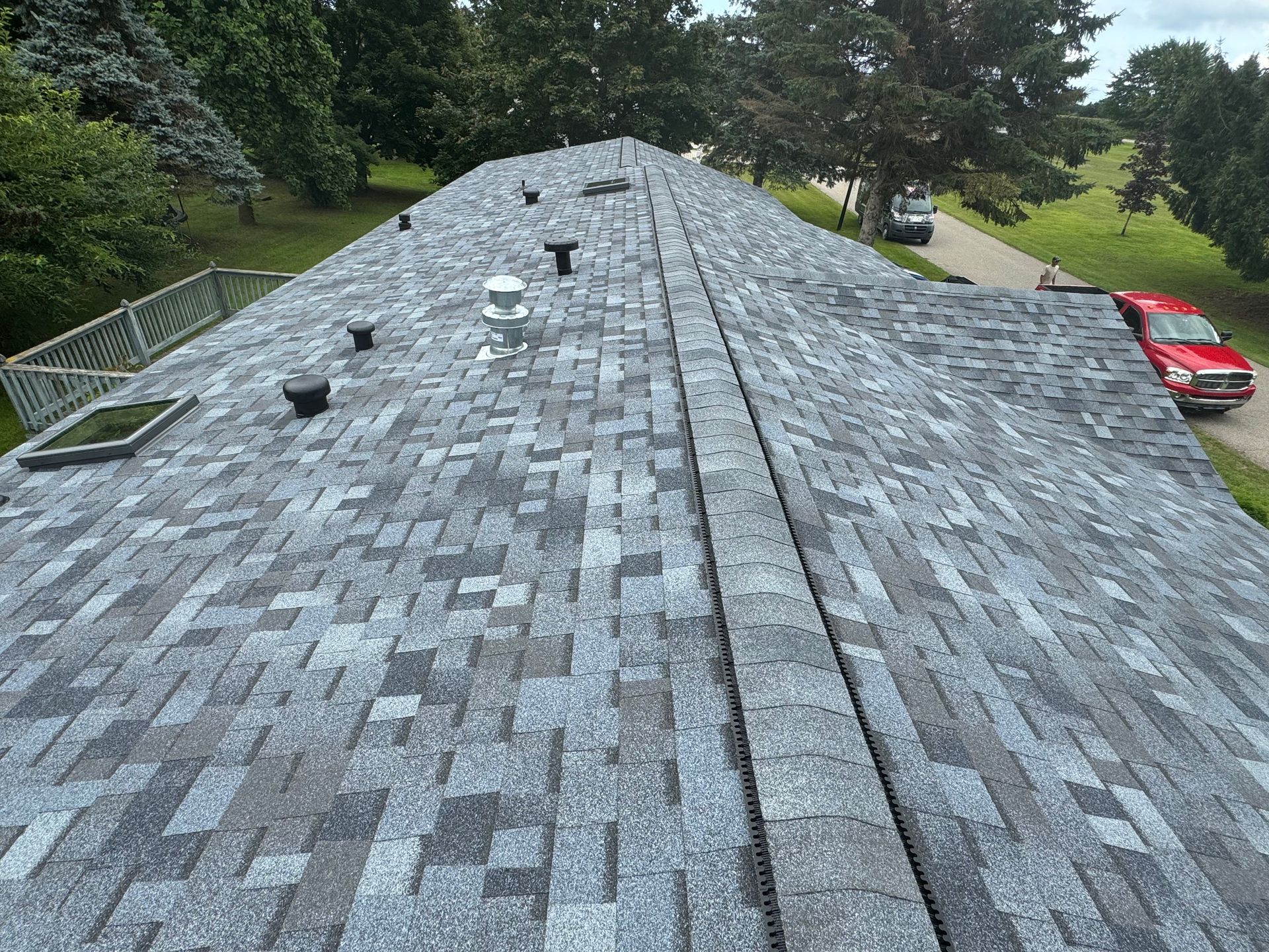 Gray asphalt shingle roof with vents, trees, and a red truck.