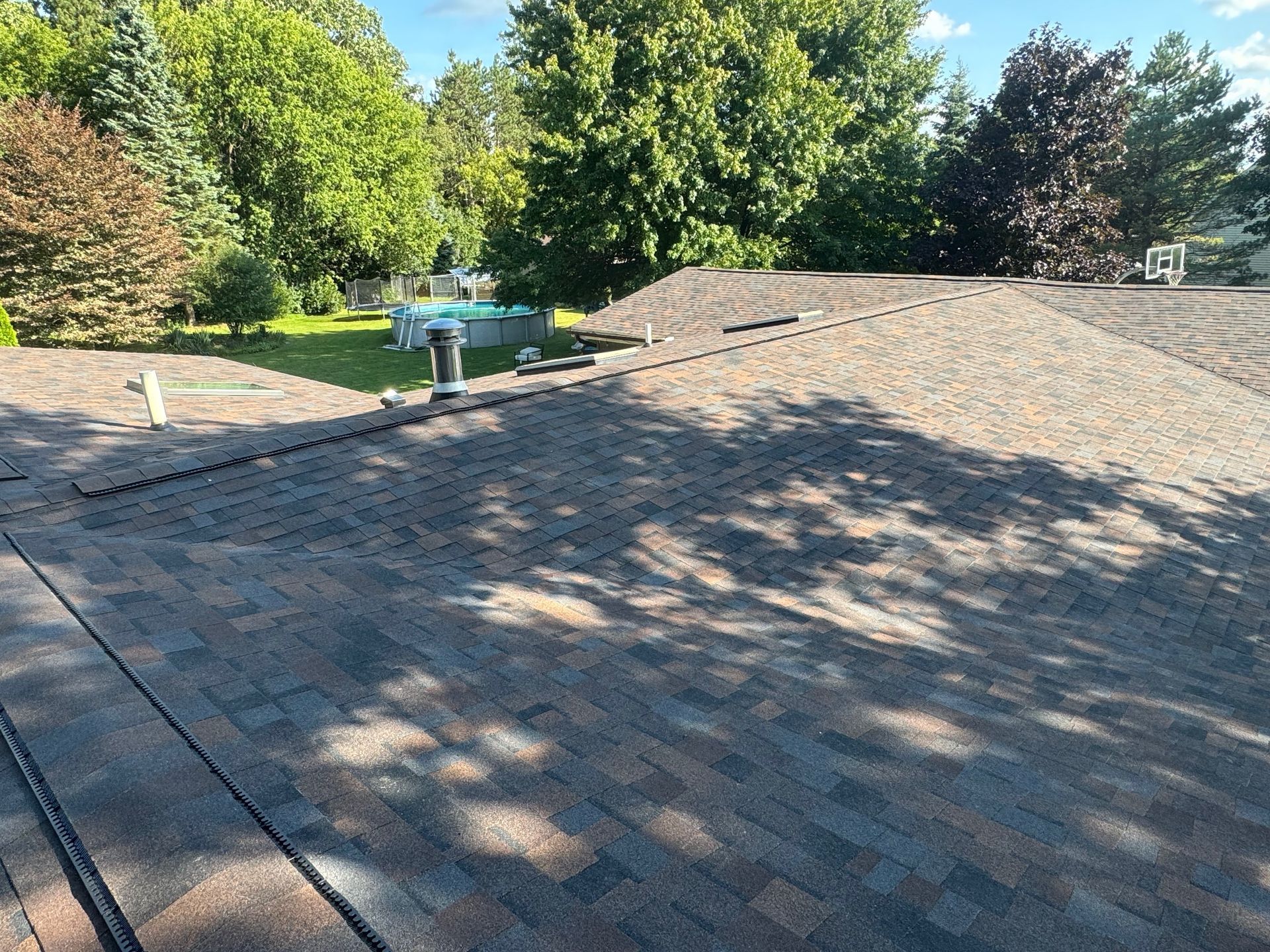 Roof with brown shingles, vents, and surrounding trees. Sunny outdoor setting.