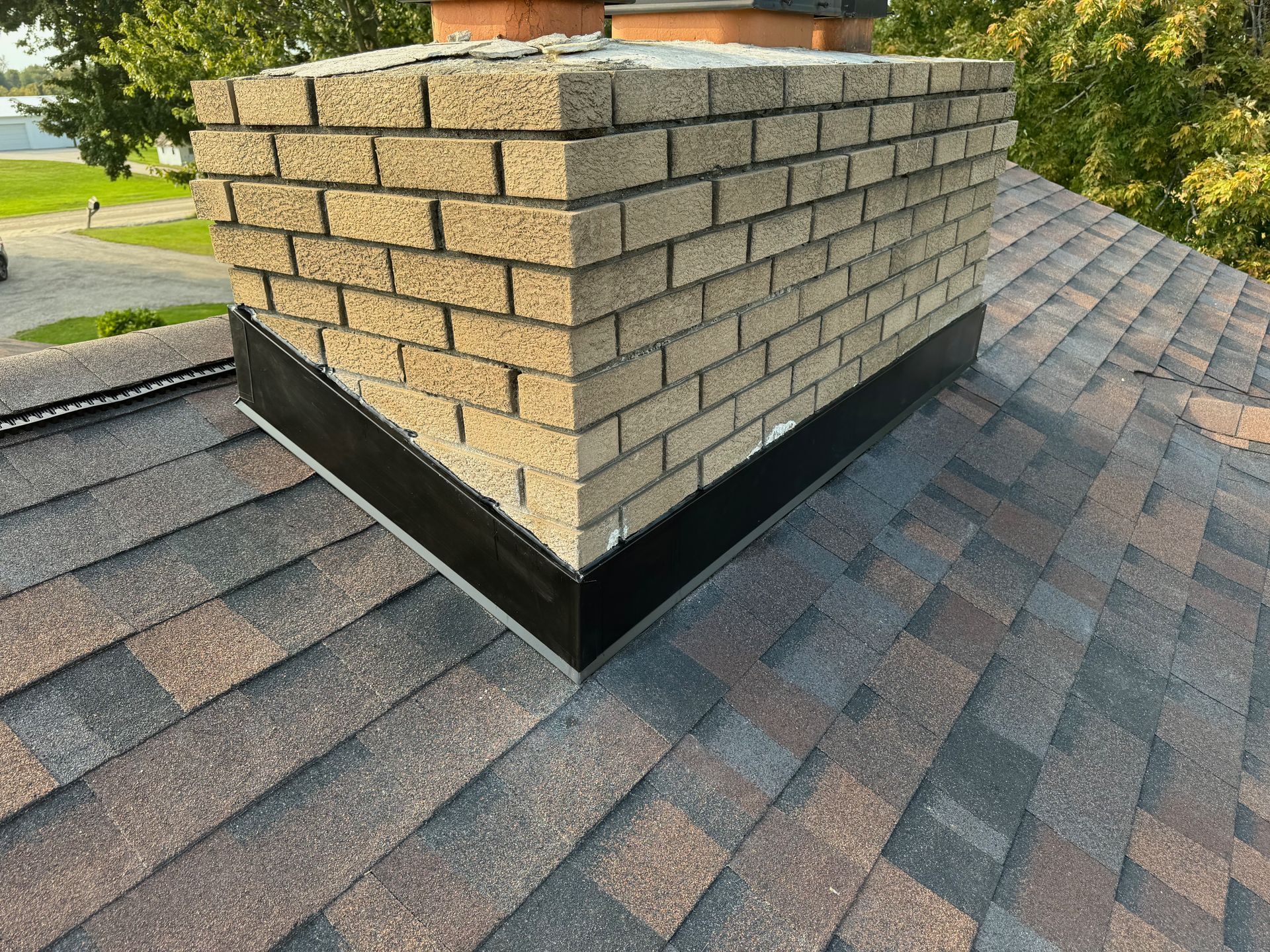 Brick chimney on a shingled roof with black flashing.