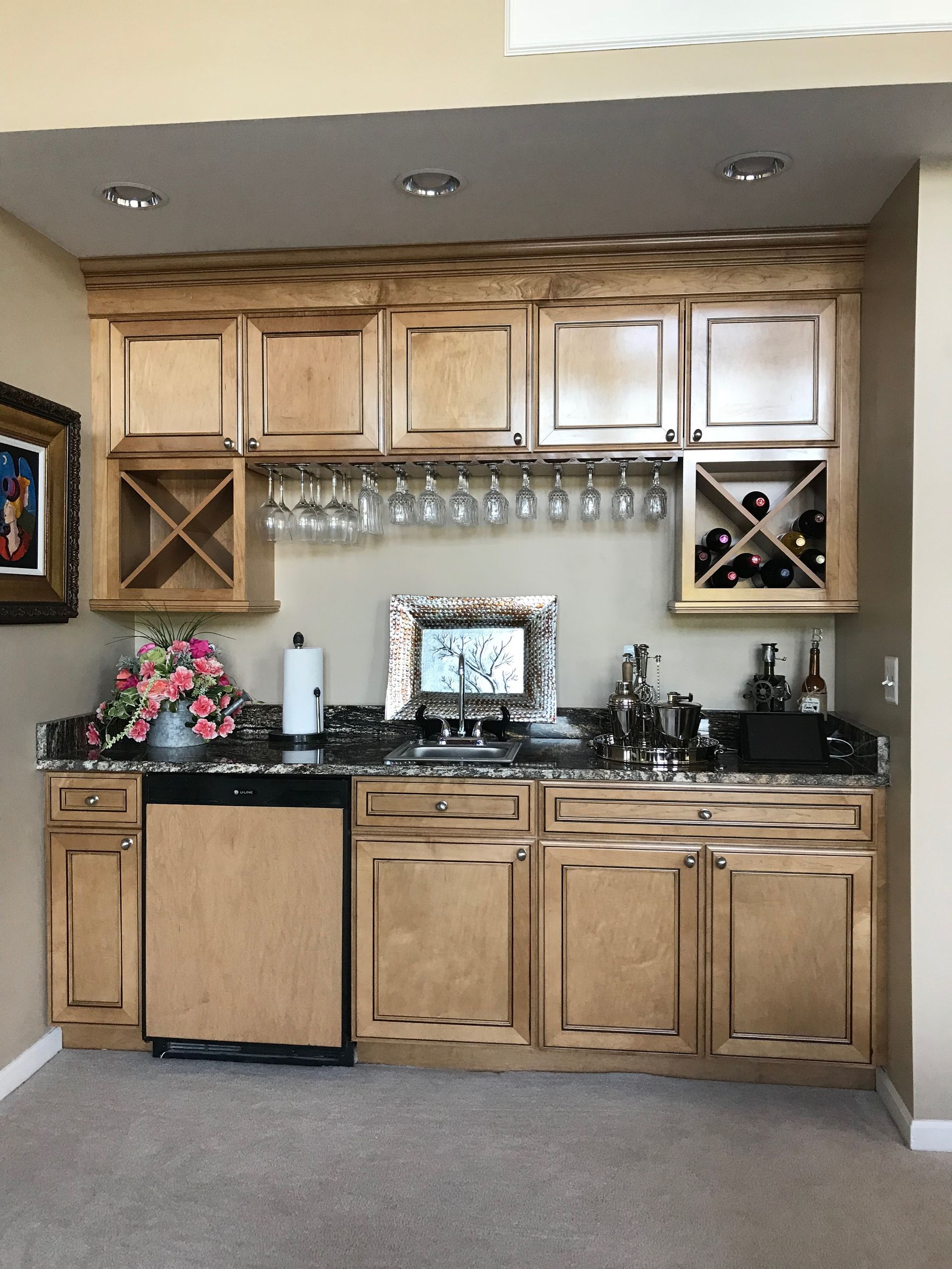 Built-in home bar with light wood cabinets, granite countertop, glassware rack, and a small sink.
