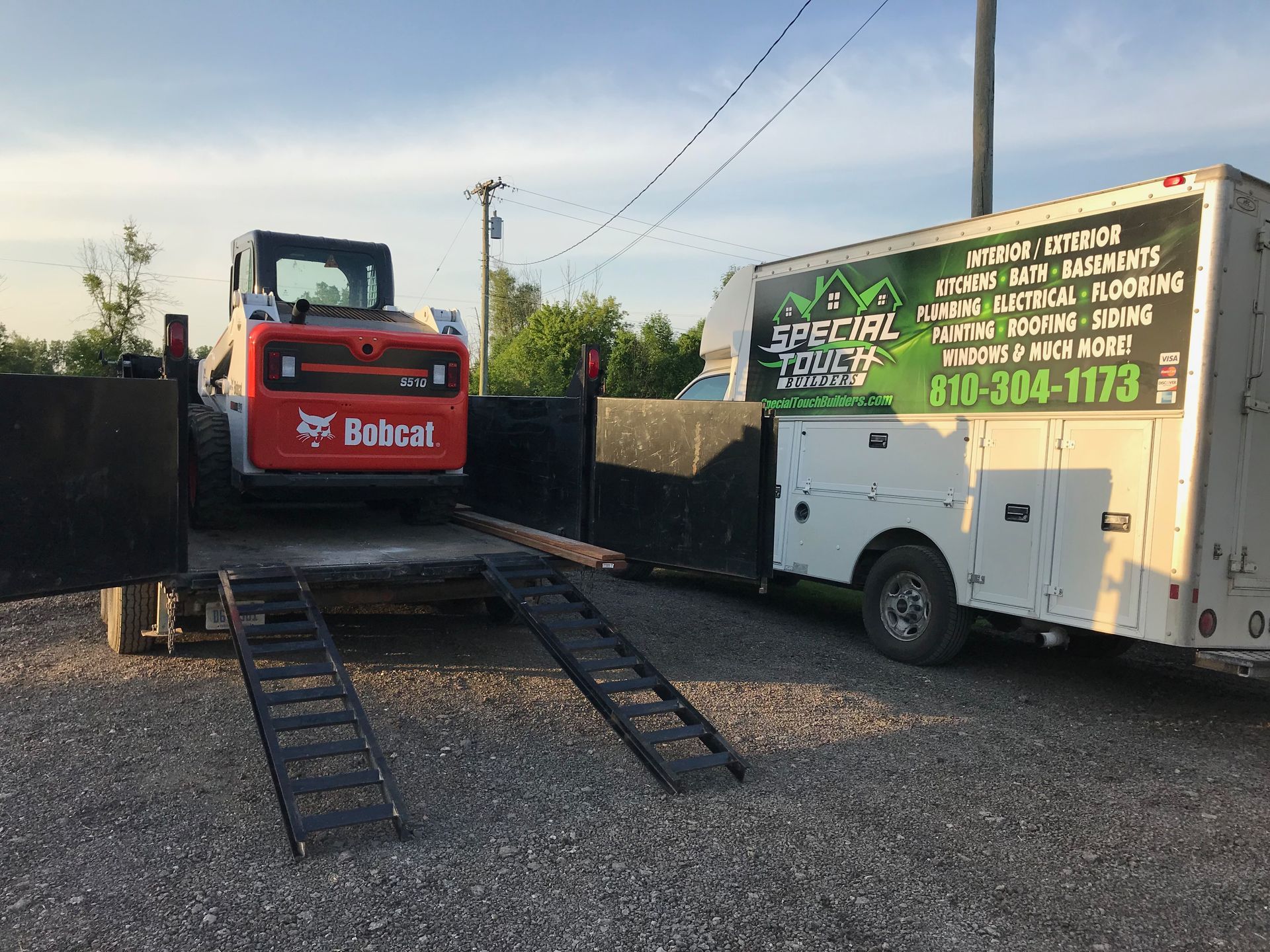 Bobcat loader on trailer next to a service truck with 