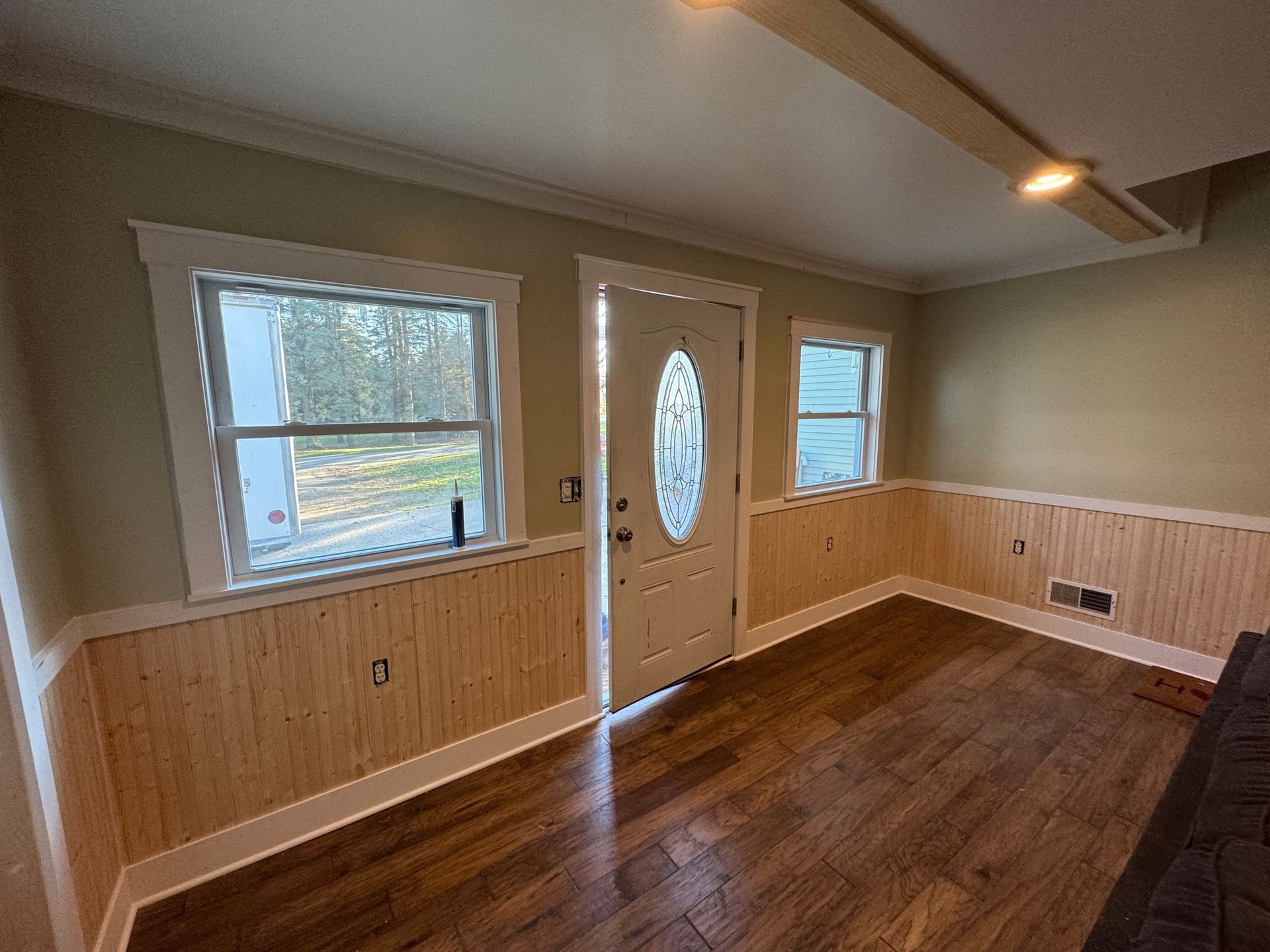 Interior room with hardwood floors, light wood paneling, white trim, and a door with an oval window.