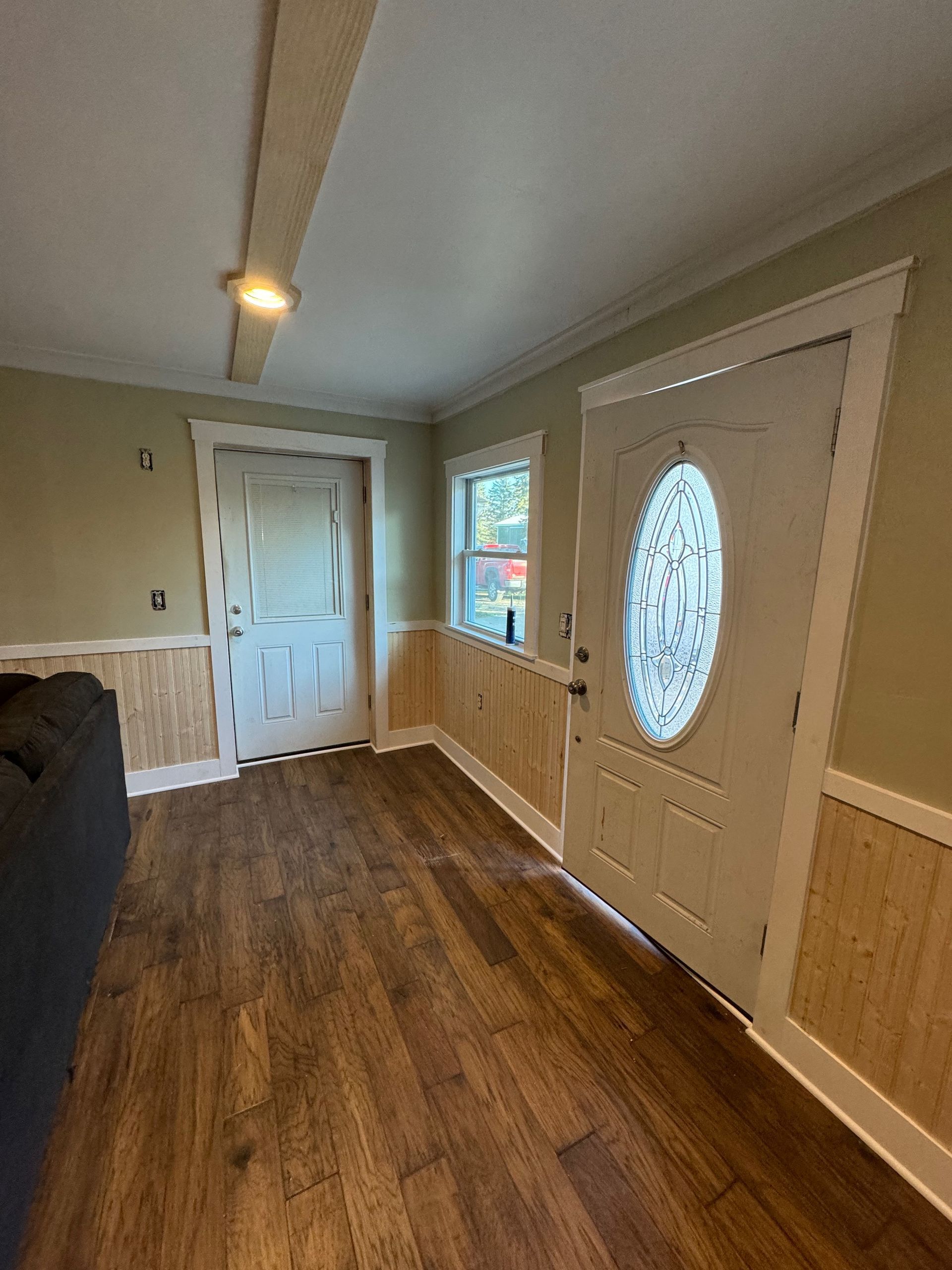 Interior view of a room with wood-look flooring, light green walls, a white door with an oval window, and wainscoting.